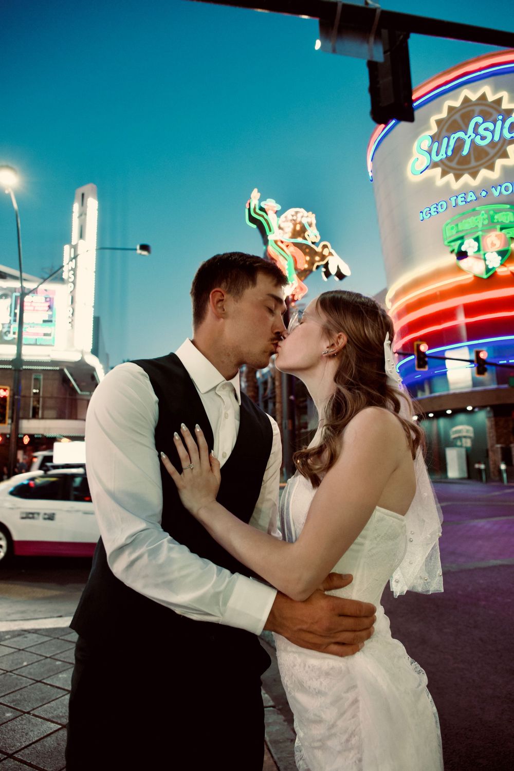 Newlywed couple sharing a kiss on the Las Vegas Strip at night with neon signs glowing behind them.