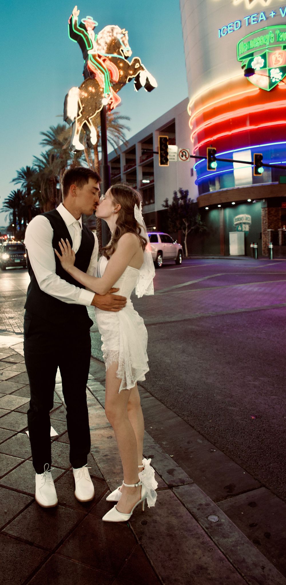 Couple kissing on Las Vegas street at night in wedding attire near neon signs.