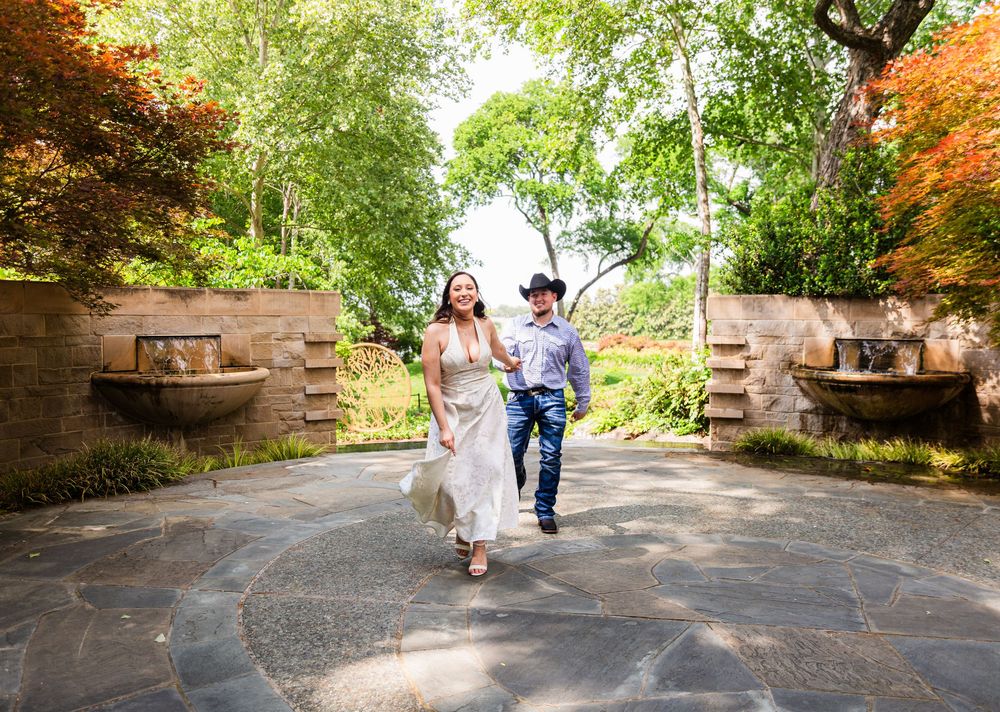 A joyful couple walks hand-in-hand through a lush garden gate surrounded by vibrant greenery and colorful foliage.