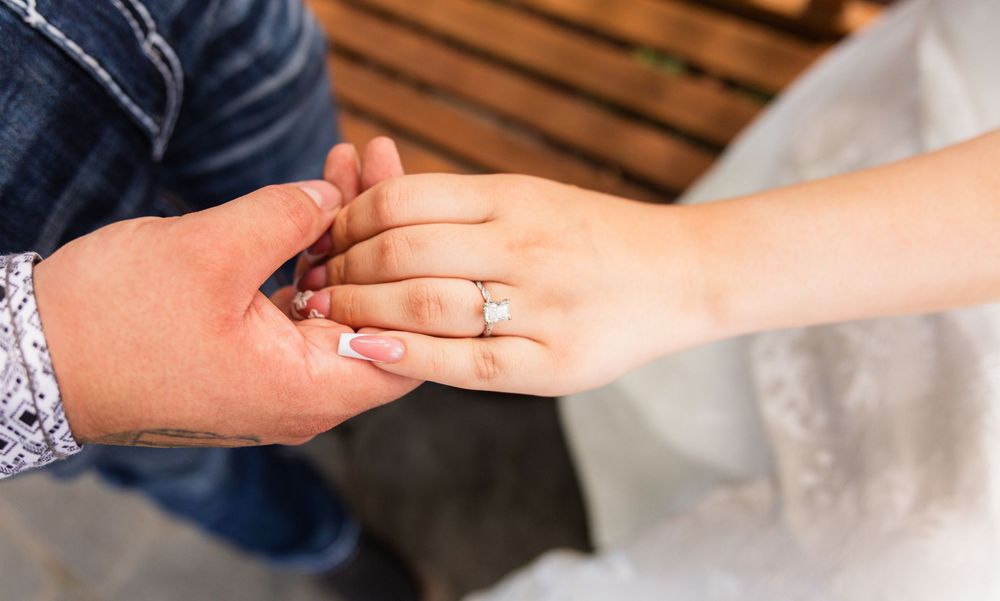 Close-up of a couple holding hands with a sparkling diamond engagement ring on the bride's finger.