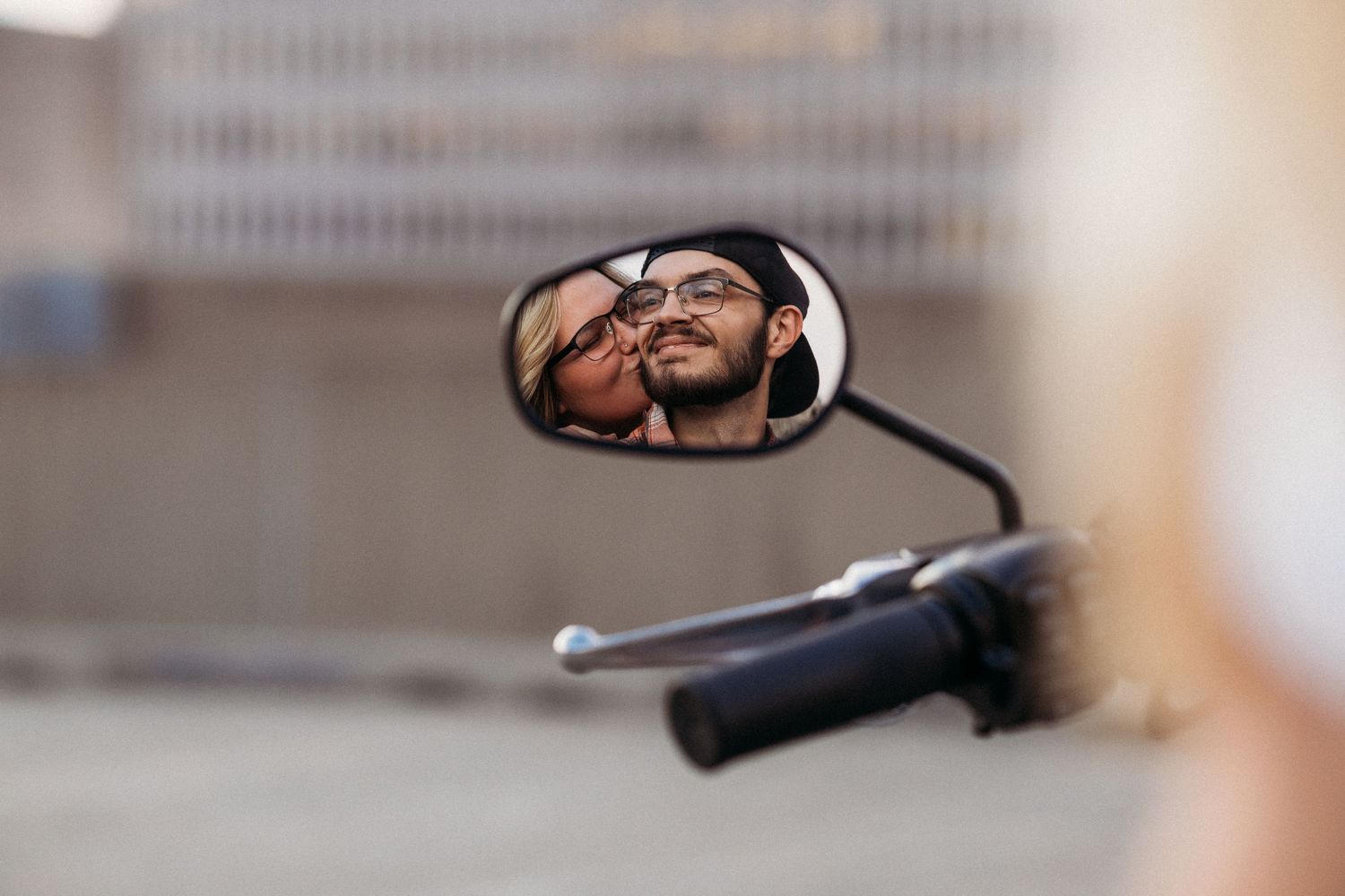 Couple reflected in a motorcycle side mirror, sharing a romantic moment on a city street.