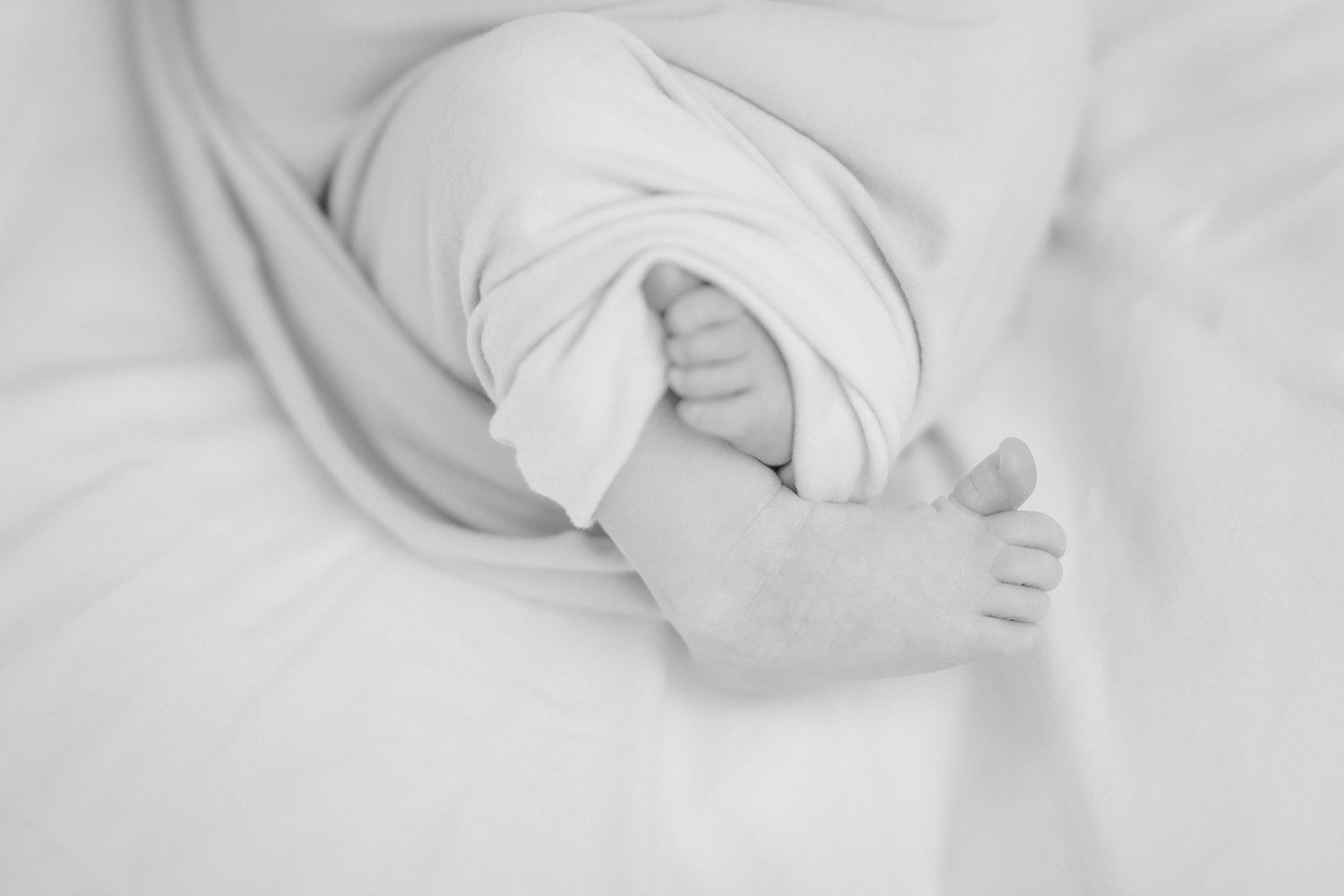 Newborn baby sleeping peacefully on a knit blanket wearing a plaid newsboy cap and beige wrap outfit.