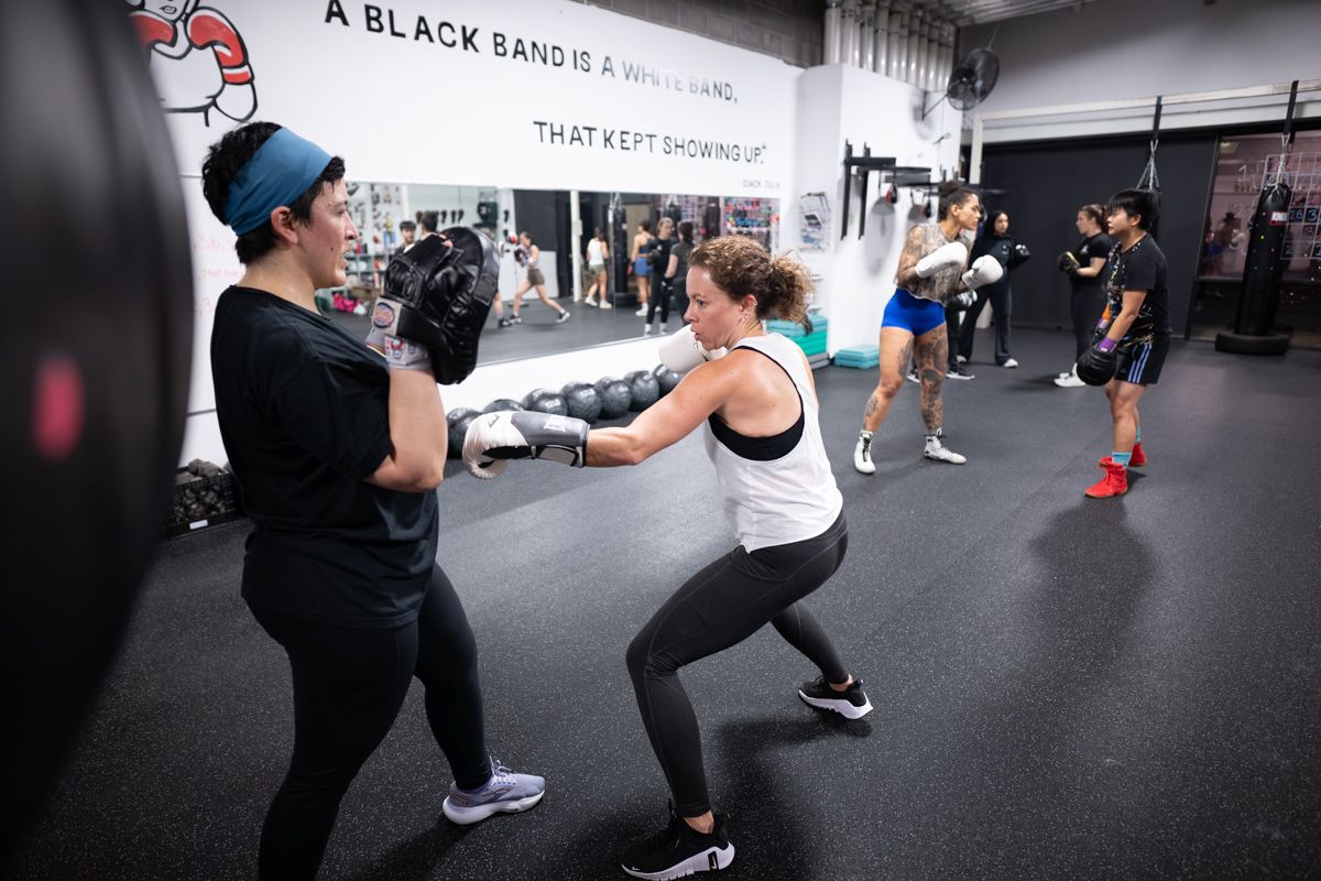 Two women practicing boxing drills in a gym with a motivational sign on the wall.