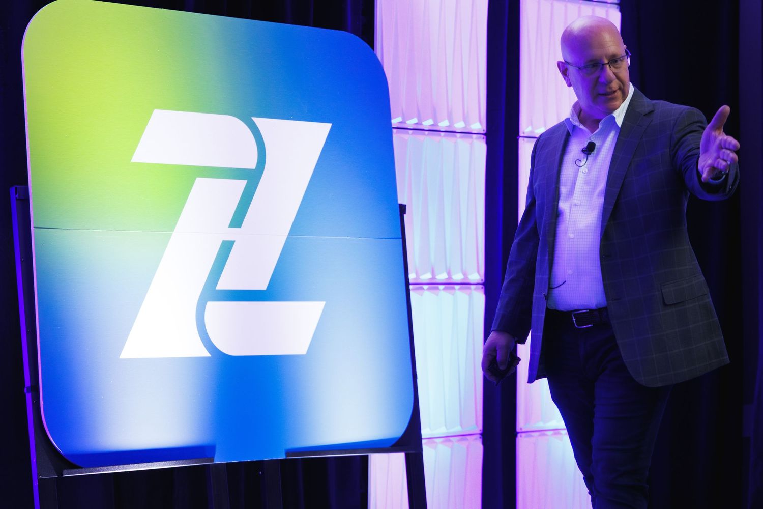 alt="Corporate keynote speaker presenting on stage beside large Zips Car Wash logo display at business conference Orlando"