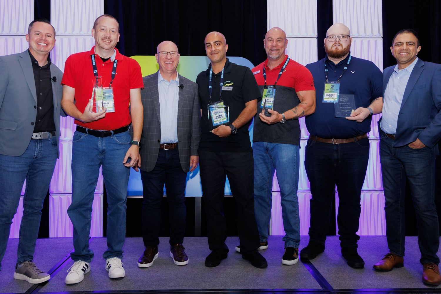 alt="Award recipients holding trophies on stage with executives at Zips Car Wash corporate conference ceremony in Orlando Florida"