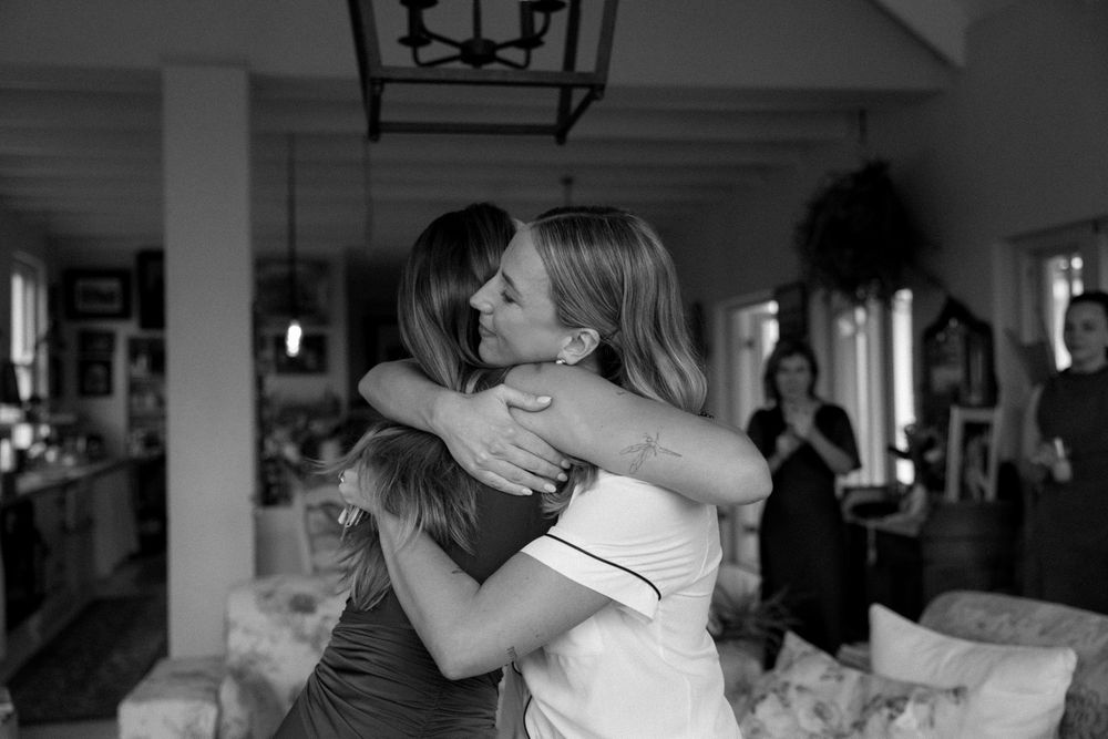 Black and white photo of bride sharing emotional hug with guest at indoor wedding celebration.