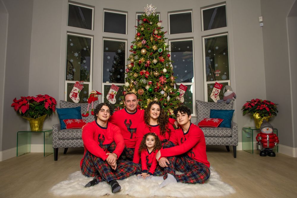 Family of five in matching red Christmas outfits posing together in front of a decorated holiday tree.