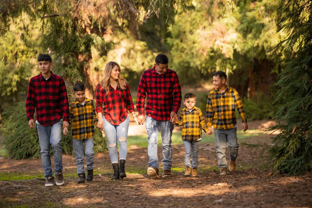 Family of six walking together along a wooded path in coordinated red and yellow plaid outfits.