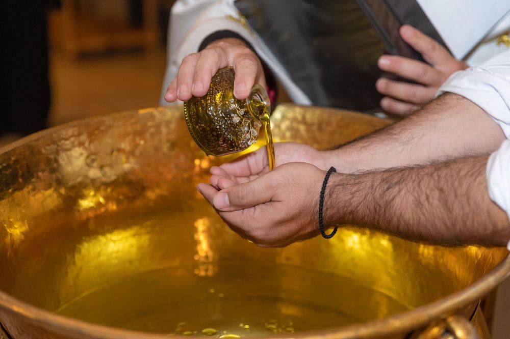 Close-up of ceremonial liquid being poured into a golden basin during a Christian baptism ceremony.