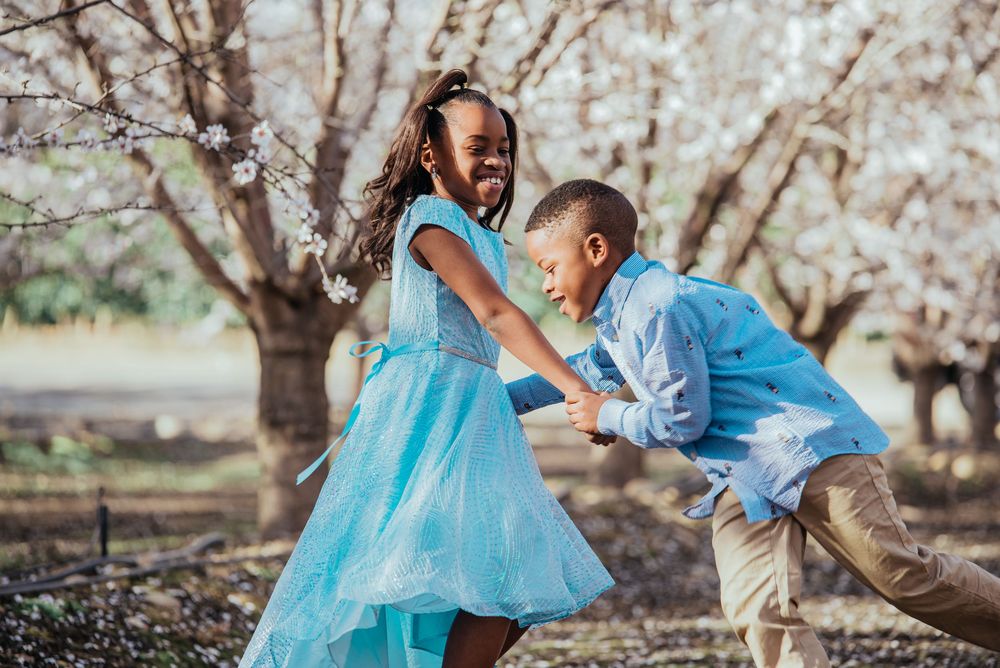 Two children laughing and playing together beneath blooming orchard trees during an outdoor portrait session.