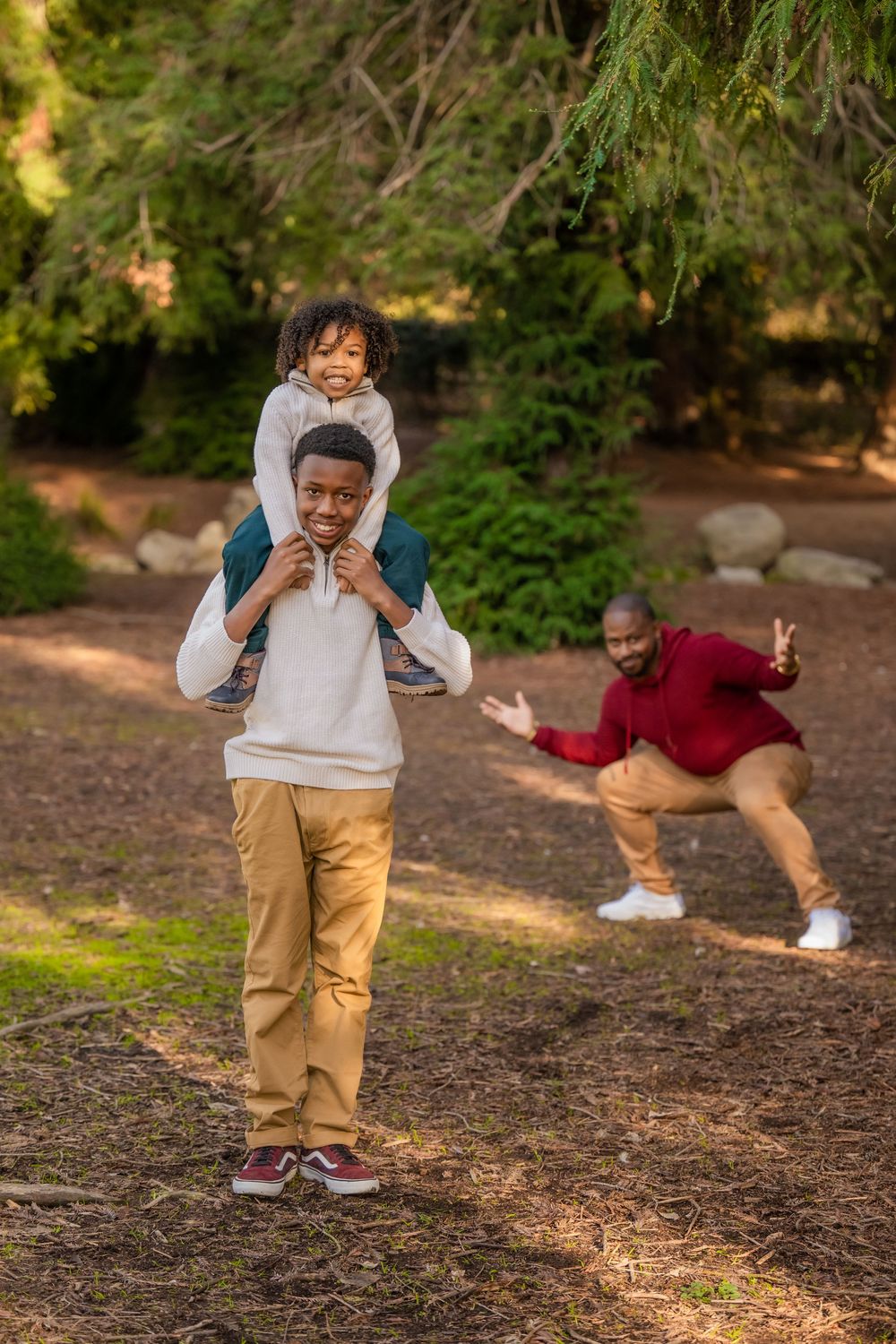 Father carrying a child on his shoulders while another child plays nearby during an outdoor family session.