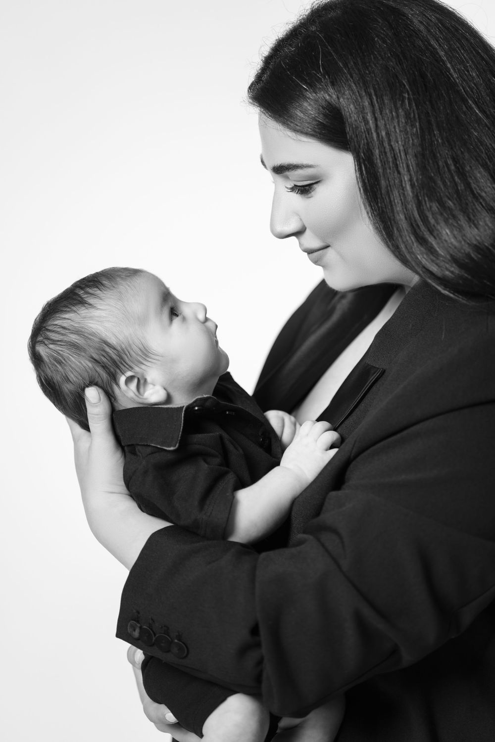 Black-and-white portrait of a mother gently cradling her newborn baby and looking lovingly into the baby's eyes.