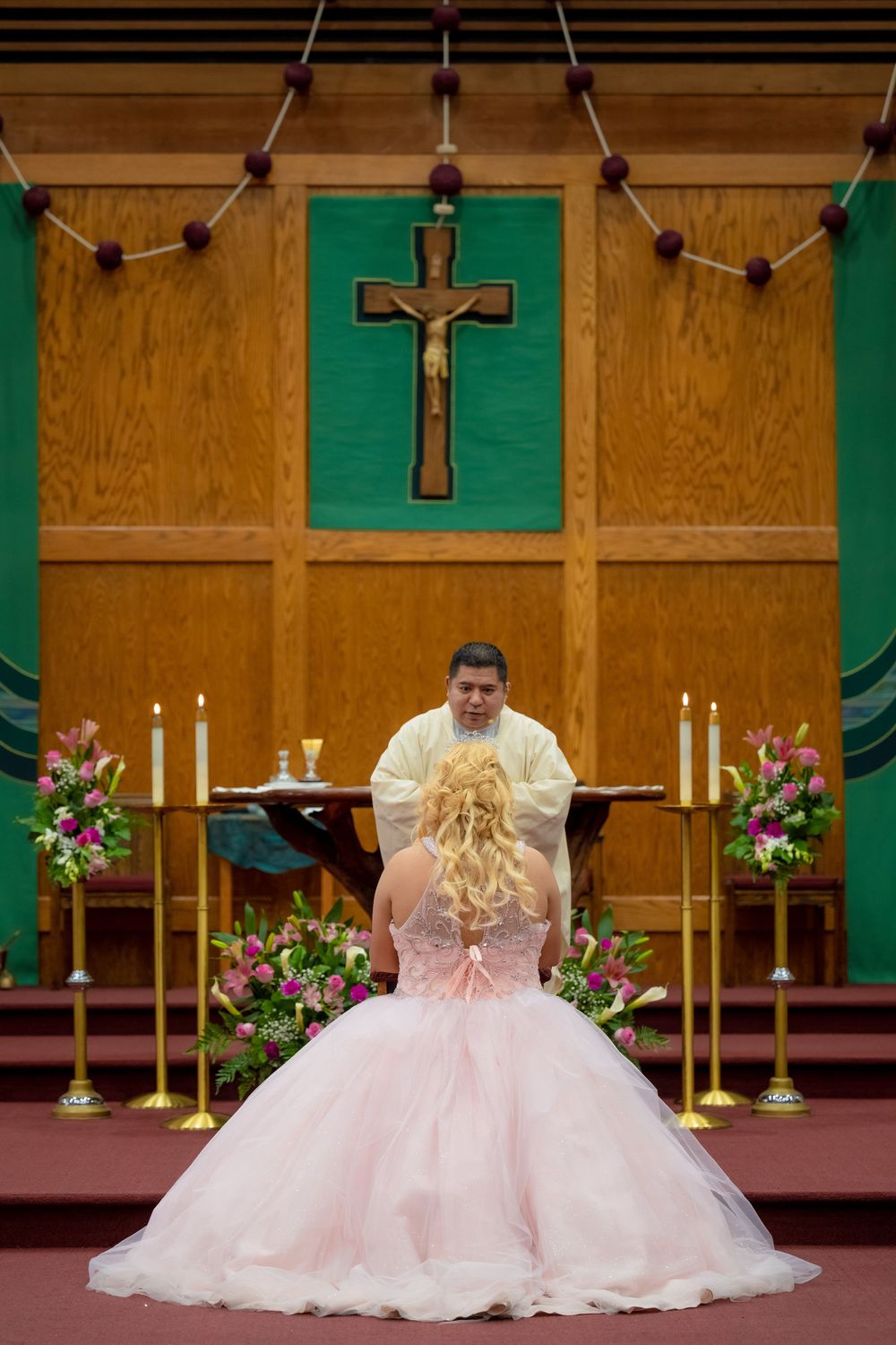 Quinceañera celebrant in a pink ball gown standing before the church altar during her religious ceremony.
