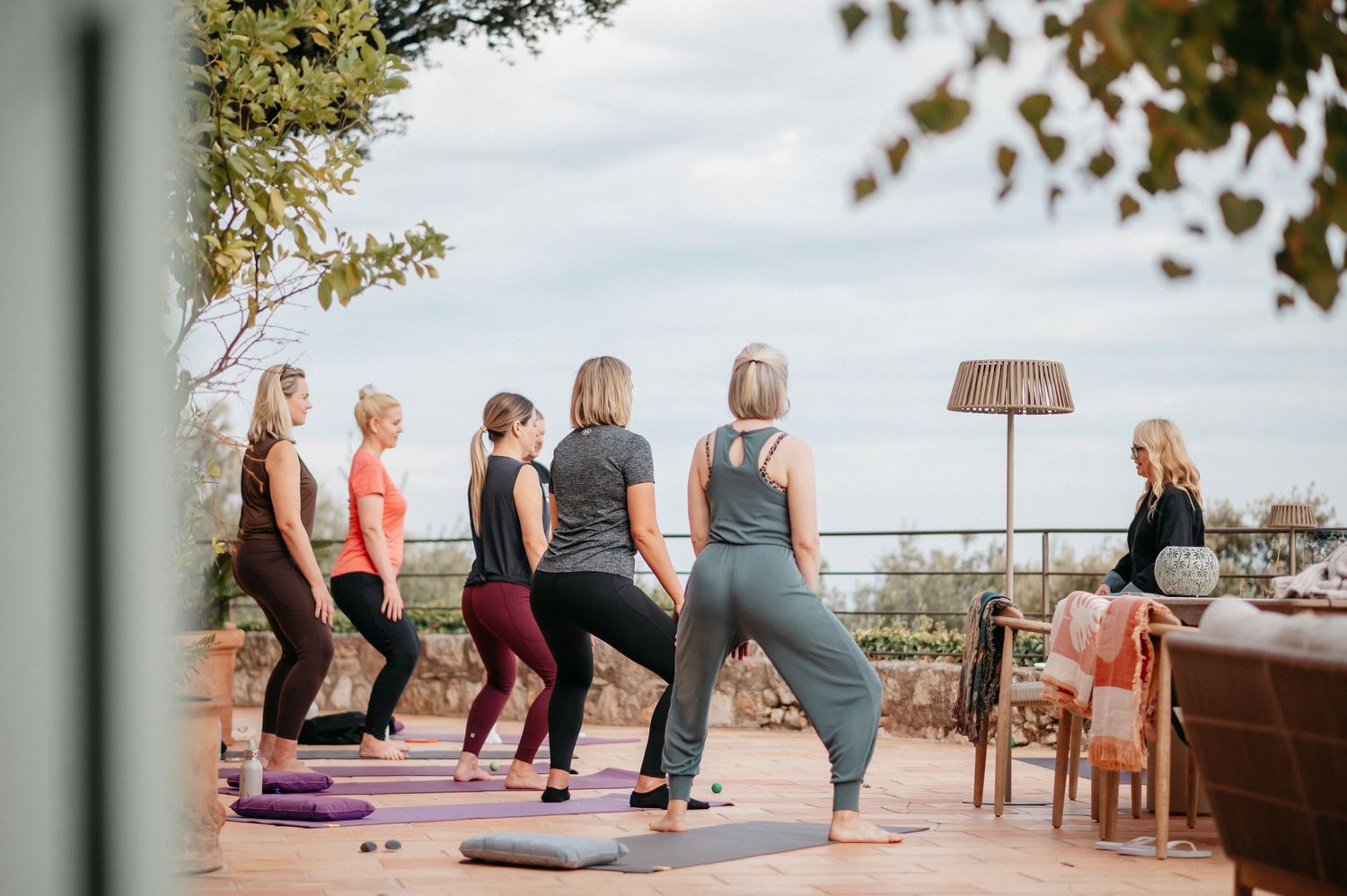 Women practicing yoga poses on an outdoor terrace with scenic views during a group yoga class.