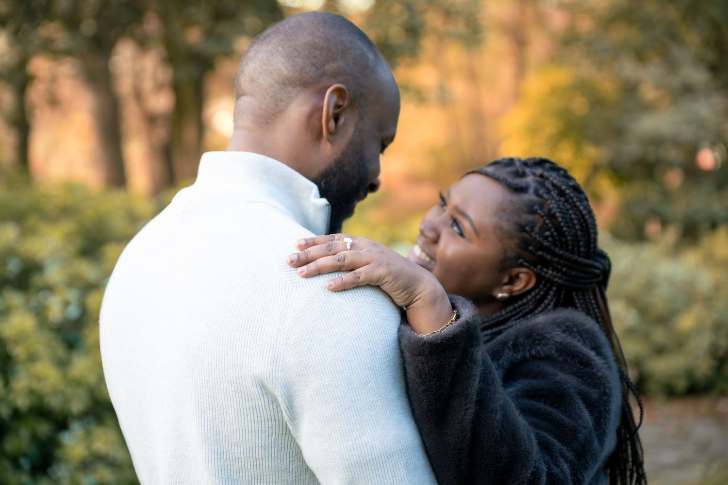 A couple shares a tender moment outdoors, the woman is resting her hand on the man's shoulder in autumn light with her Engagement ring