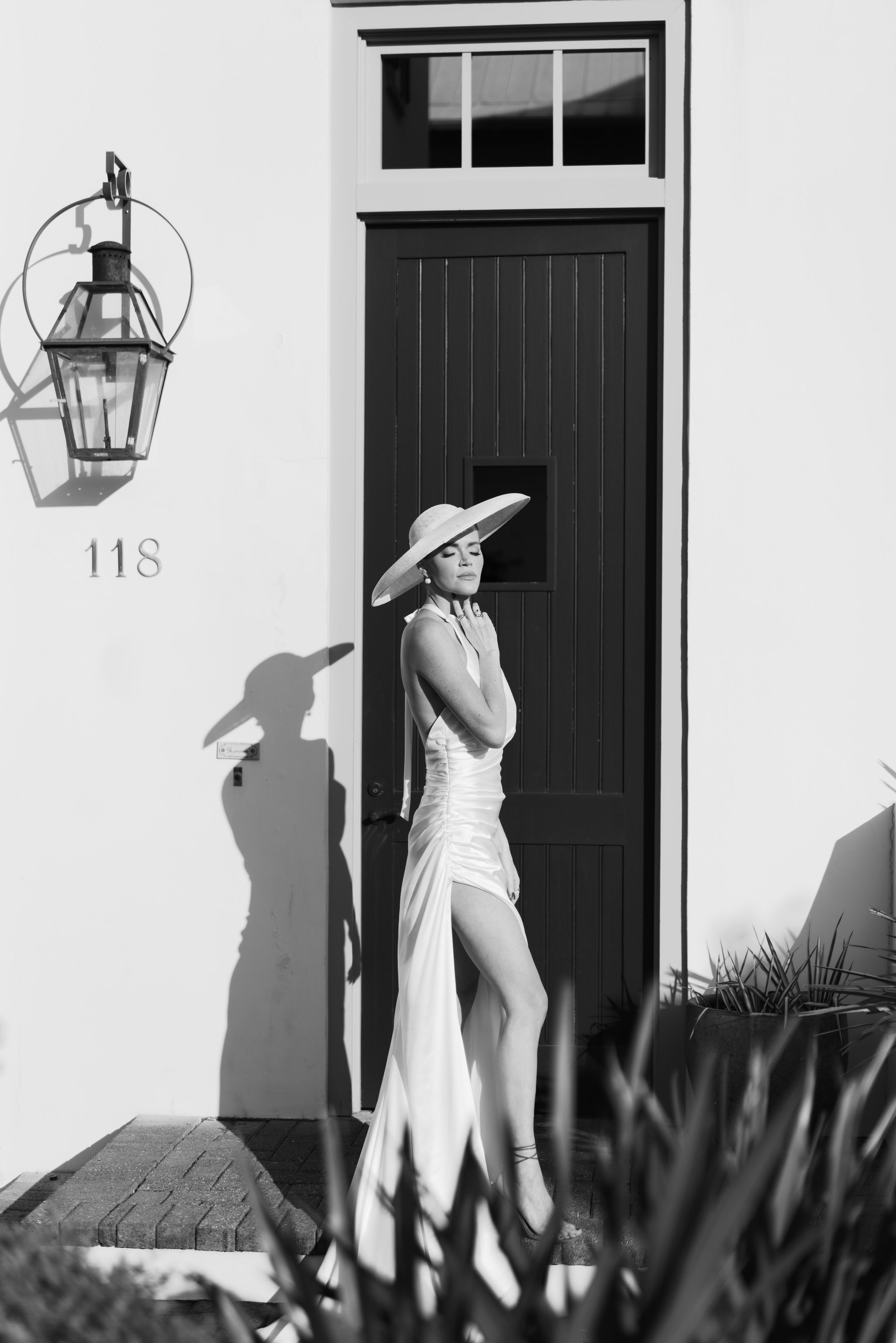 Elegant bride in white satin gown and sun hat posing by door number 118.