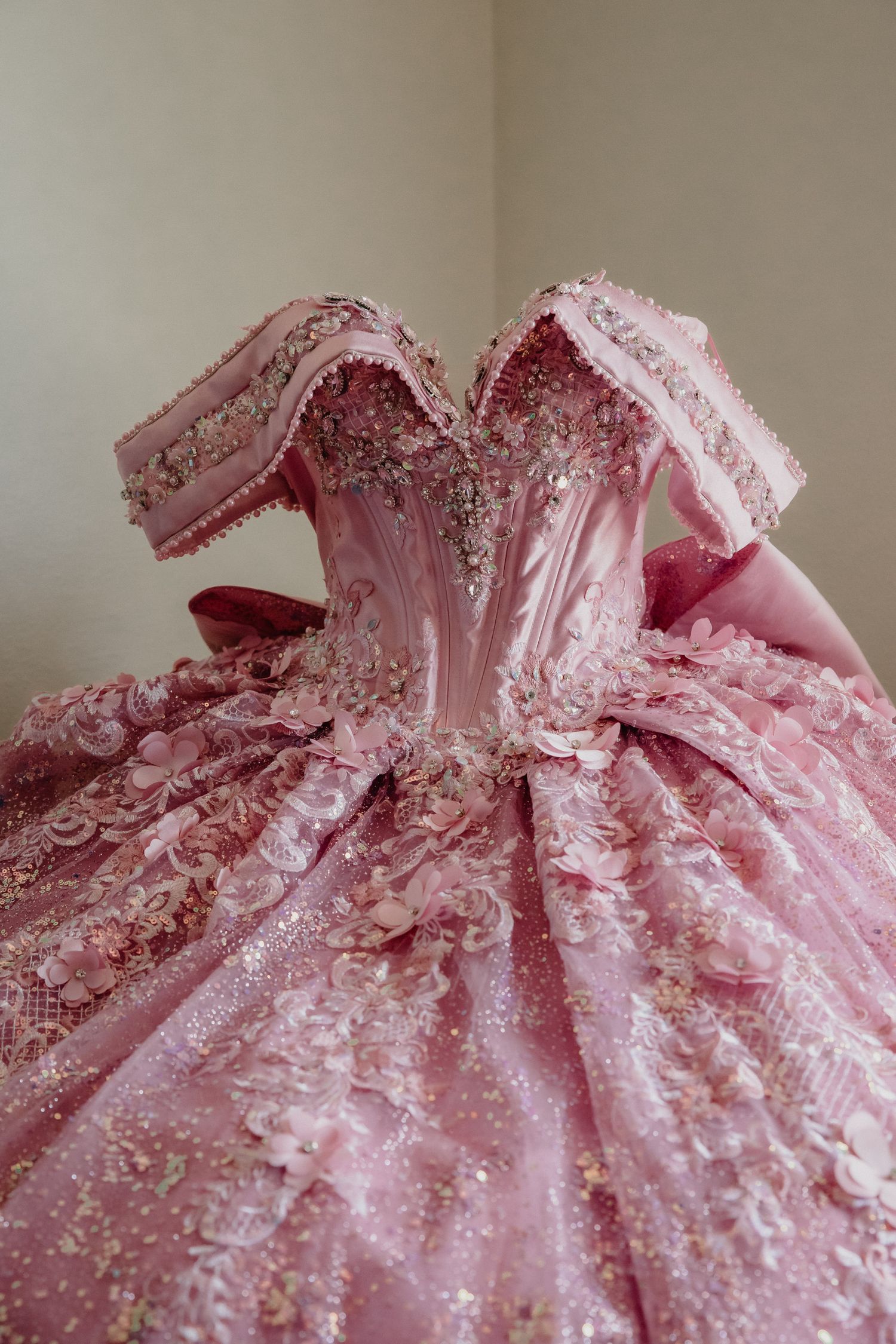Elaborate pink quinceañera ball gown with intricate beading, sequins, and floral lace embellishments on a dress form.
