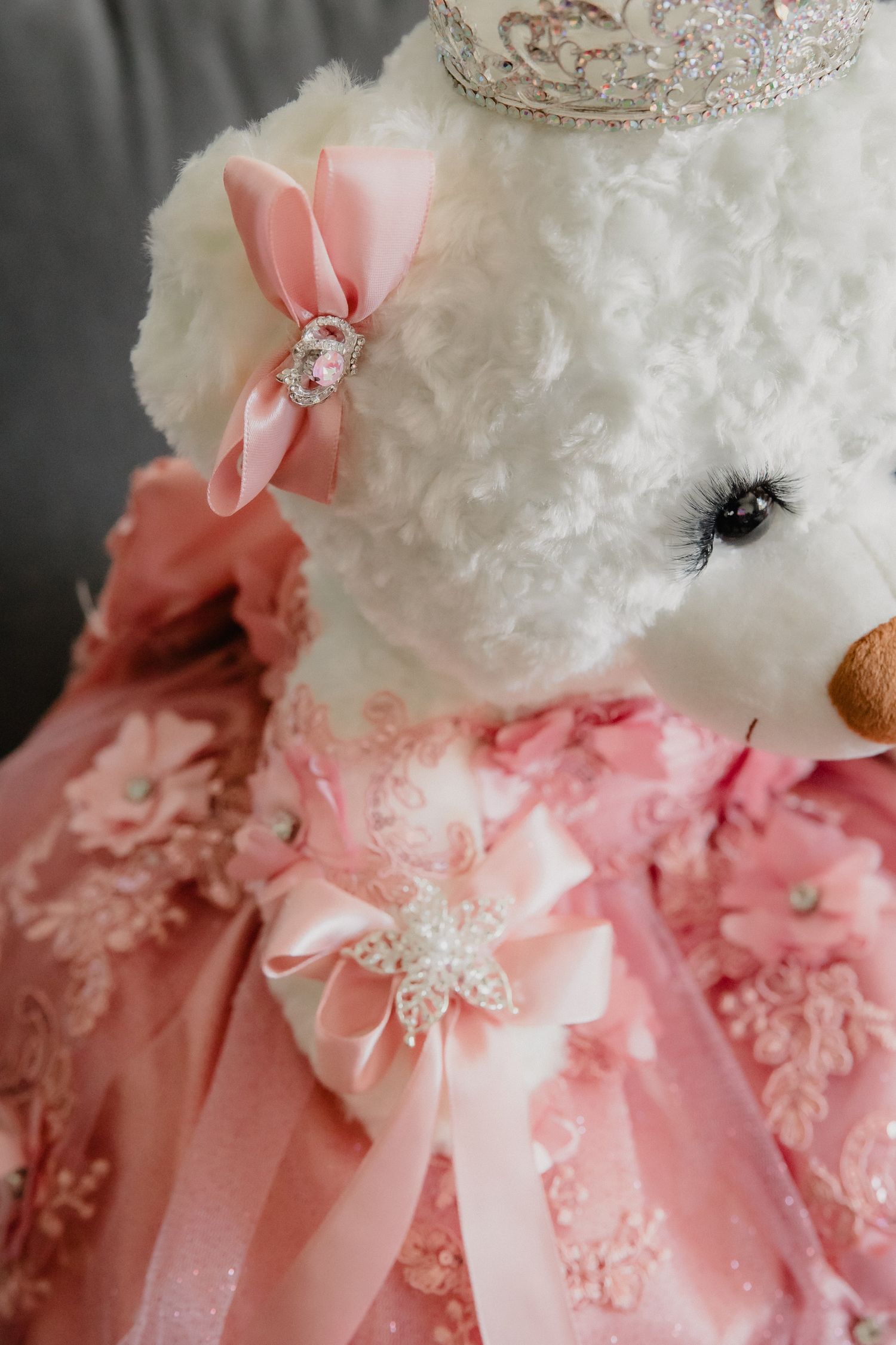 White teddy bear dressed in pink lace gown with bow and silver crown for a quinceañera celebration.