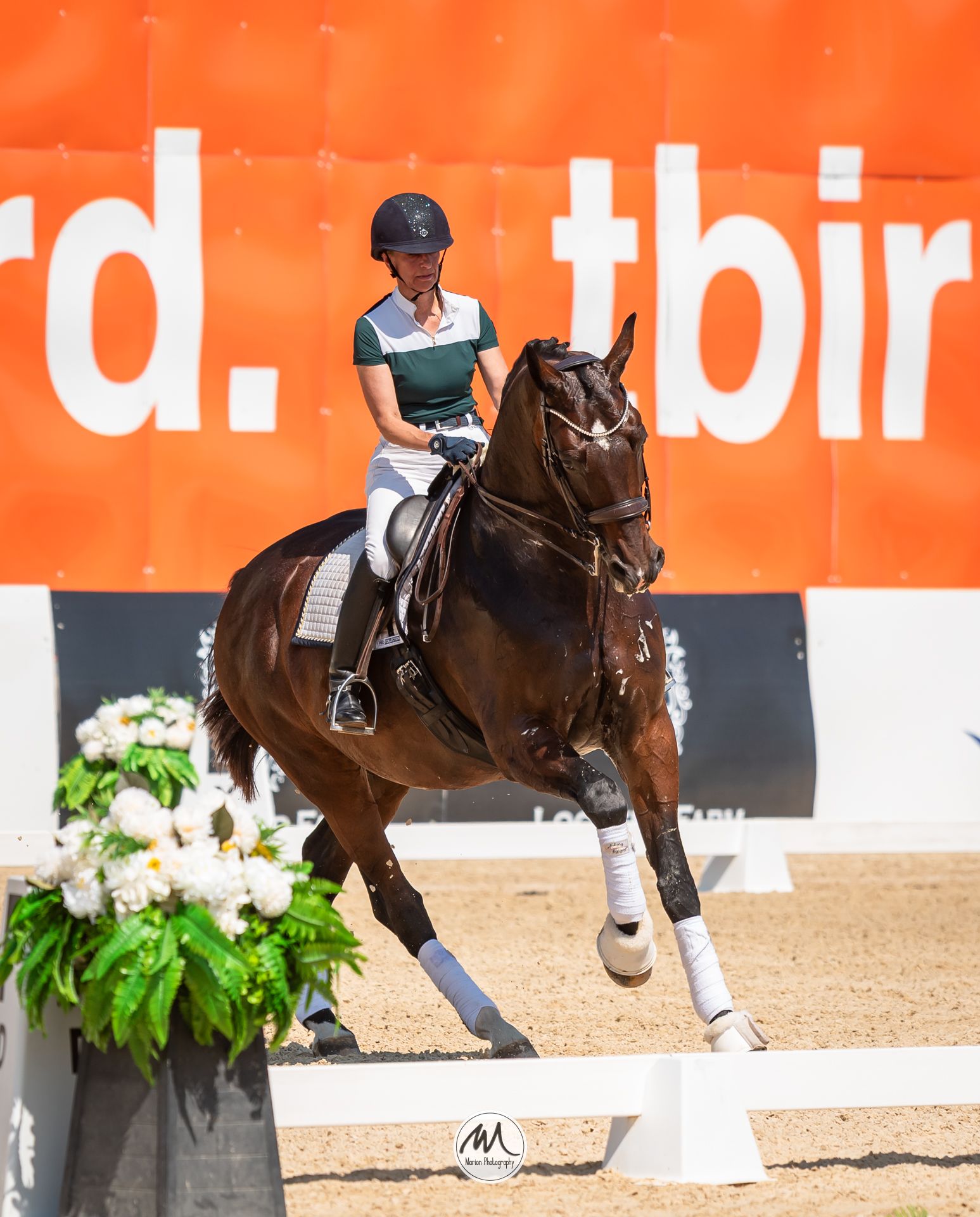 Equestrian rider in green jacket and helmet performing dressage on a chestnut horse at an outdoor competition.