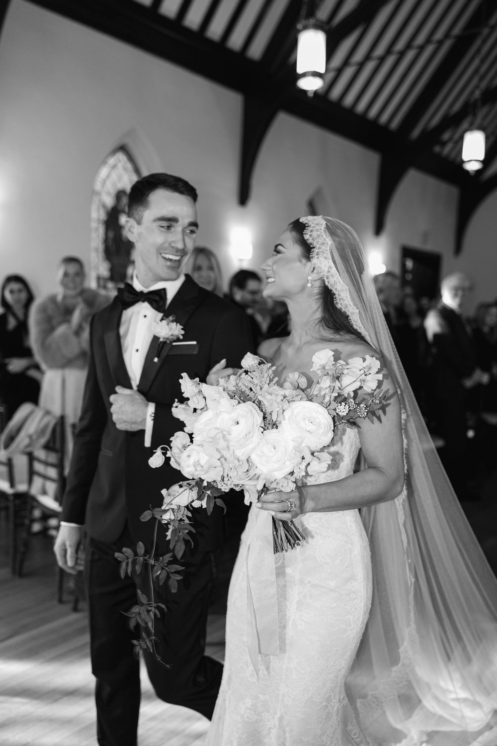 Black and white photo of a joyful bride and groom walking down the aisle after their wedding ceremony.