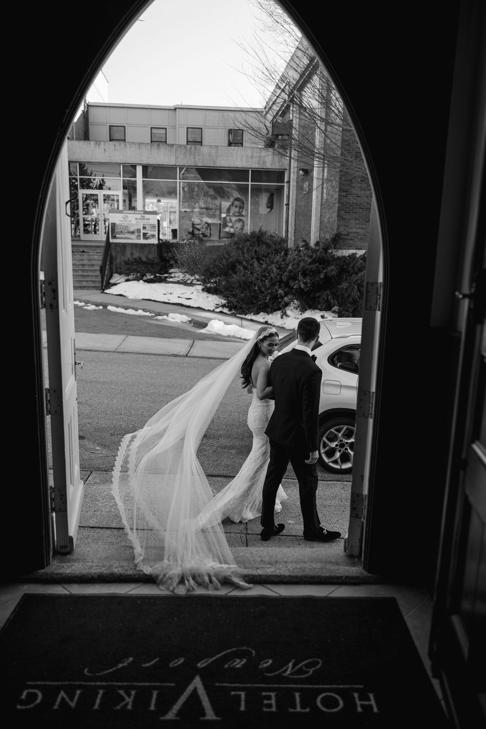 Black and white photo of bride and groom kissing in arched doorway of Hotel Viking Newport, veil flowing dramatically.