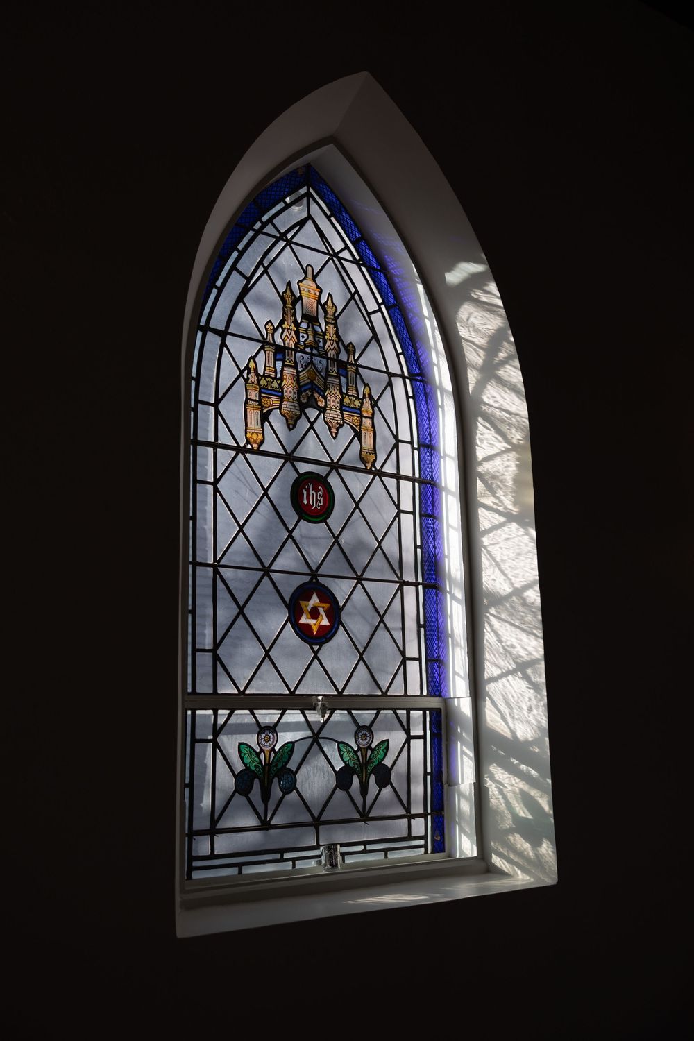Ornate stained glass church window featuring a Star of David, menorah, and floral motifs with blue border details.