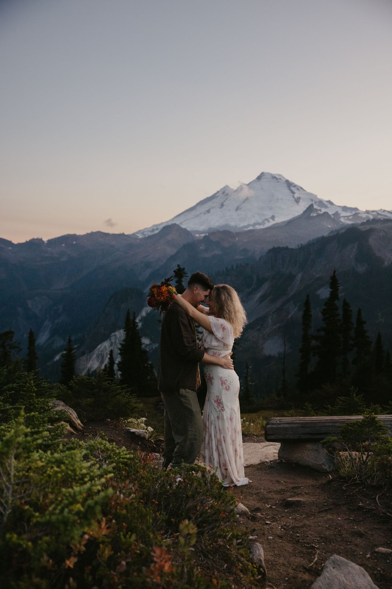 Couple embracing at sunset with snow-capped Mount Baker in background during outdoor mountain elopement ceremony.