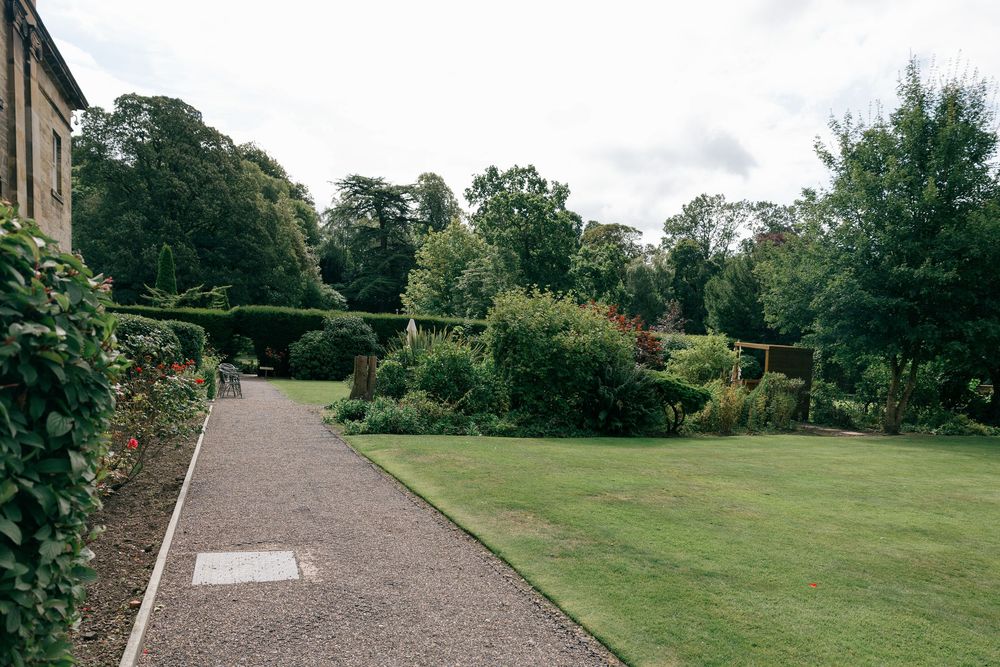 Lush garden pathway with manicured lawn, colorful shrubs, and tall trees at a scenic English country estate.