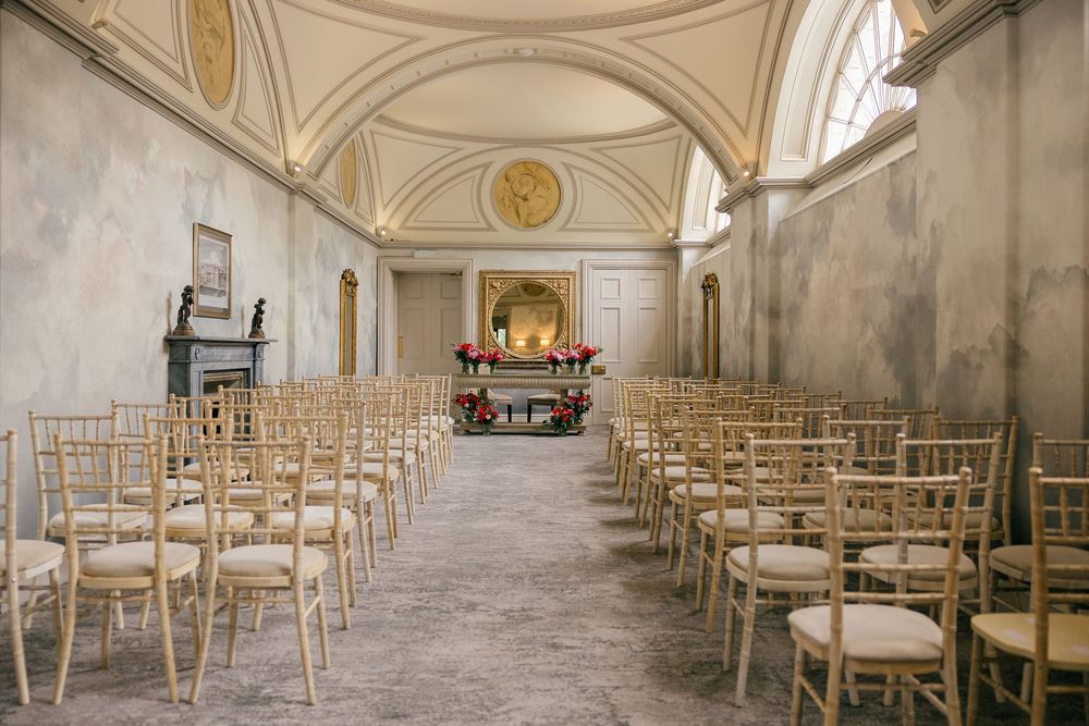 Elegant wedding ceremony hall with gold Chiavari chairs, ornate ceiling, and floral altar in a historic venue.