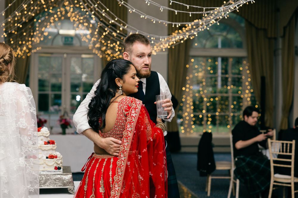 Couple shares first dance at wedding reception, bride in red embroidered lehenga, groom in suit, fairy lights backdrop.