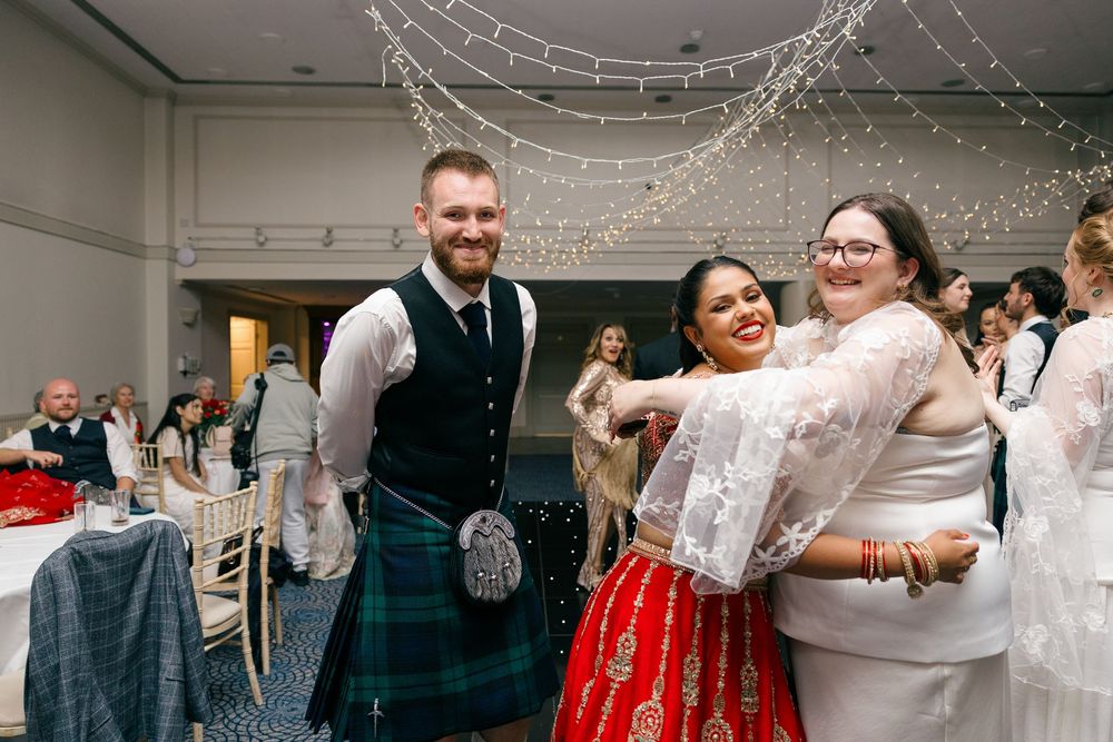 Bride and groom in Scottish kilt celebrate with guest at elegant wedding reception with fairy lights.