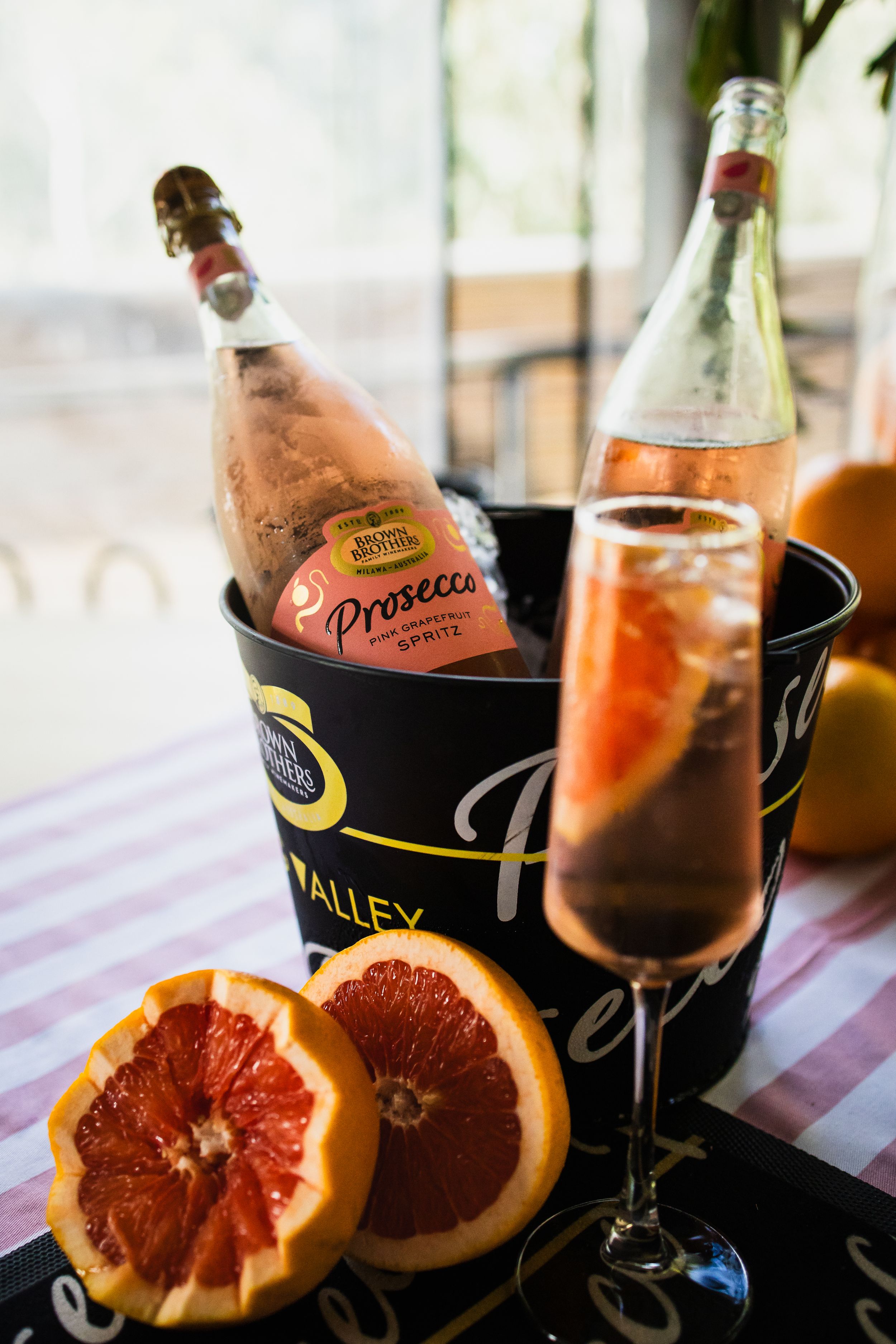 Prosecco spritz cocktail in champagne flute with grapefruit slices and chilled bottles in ice bucket on striped tablecloth.