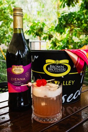 Brown Brothers Cienna Velvet Chocolate wine bottle beside a cocktail garnished with cherries and an ice bucket.