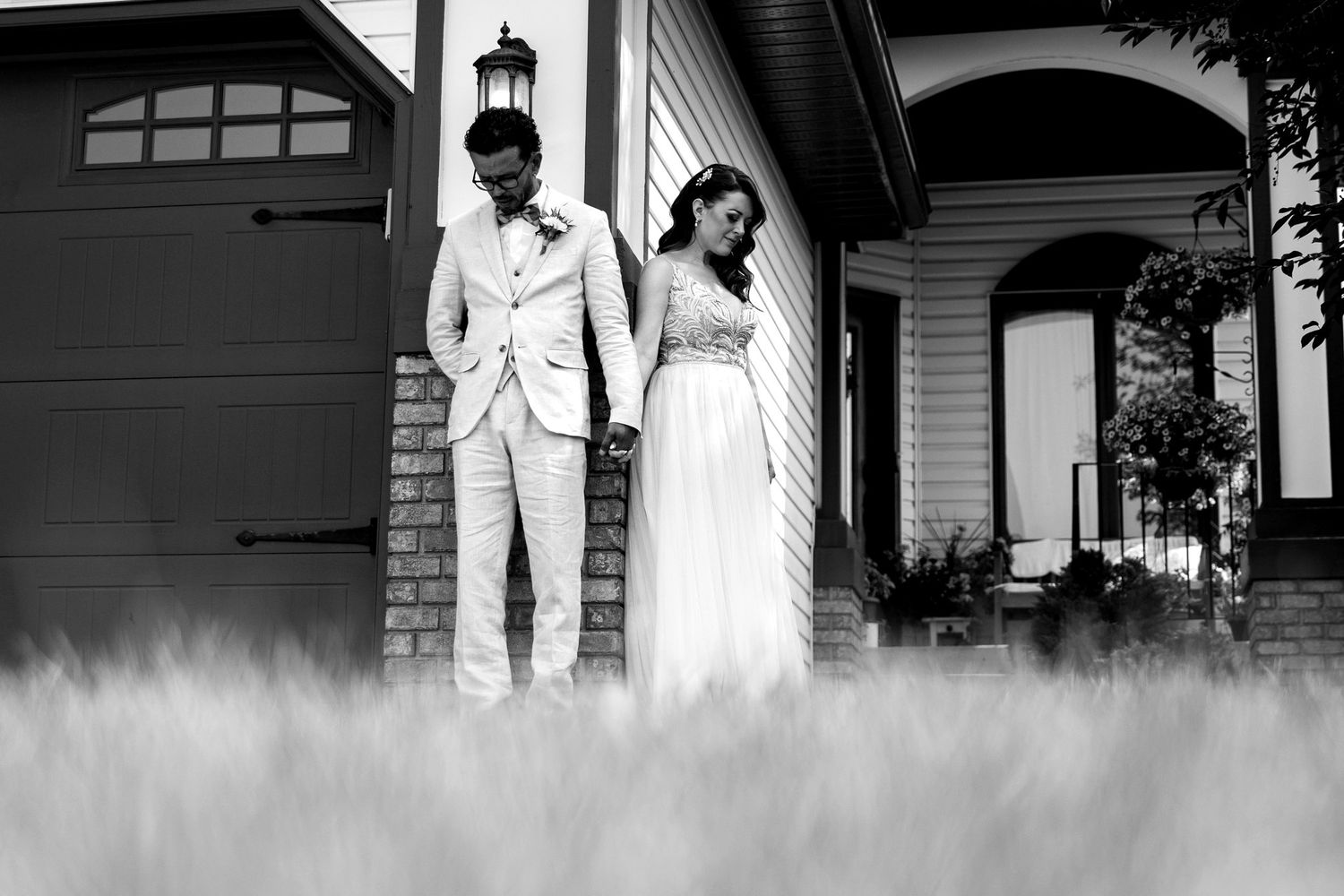 Black and white photo of the bride and groom holding hands with heads bowed in prayer outside the house