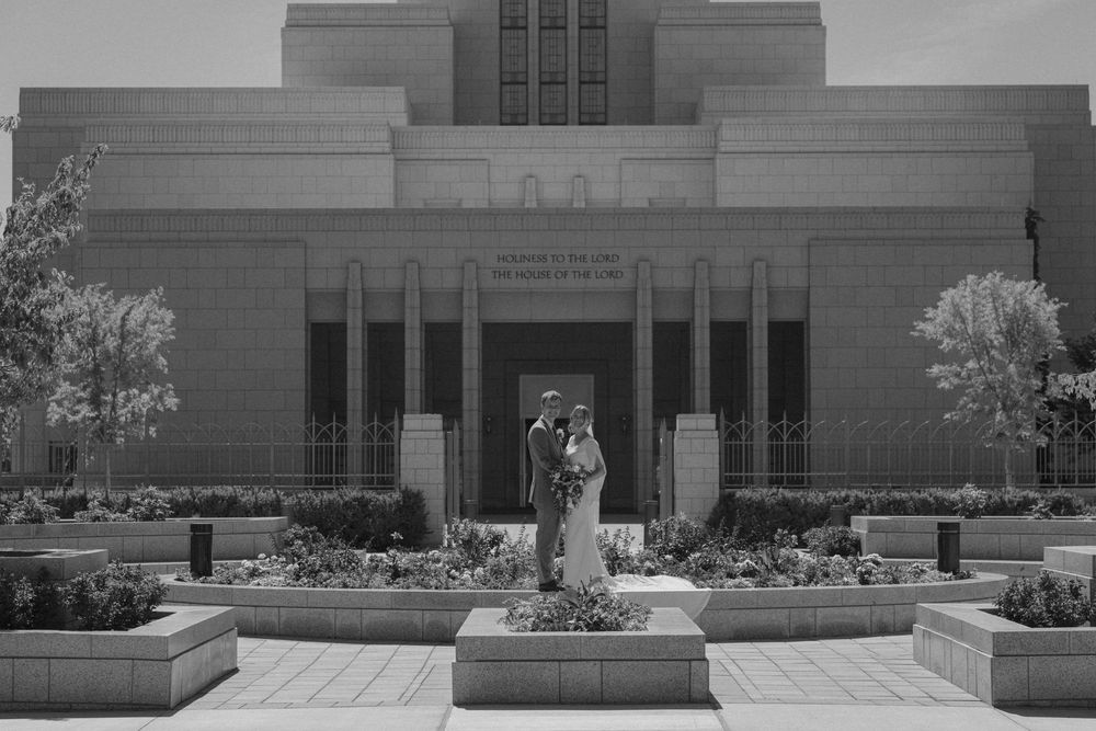 Black and white photo of a couple posing in front of an LDS temple with manicured gardens.