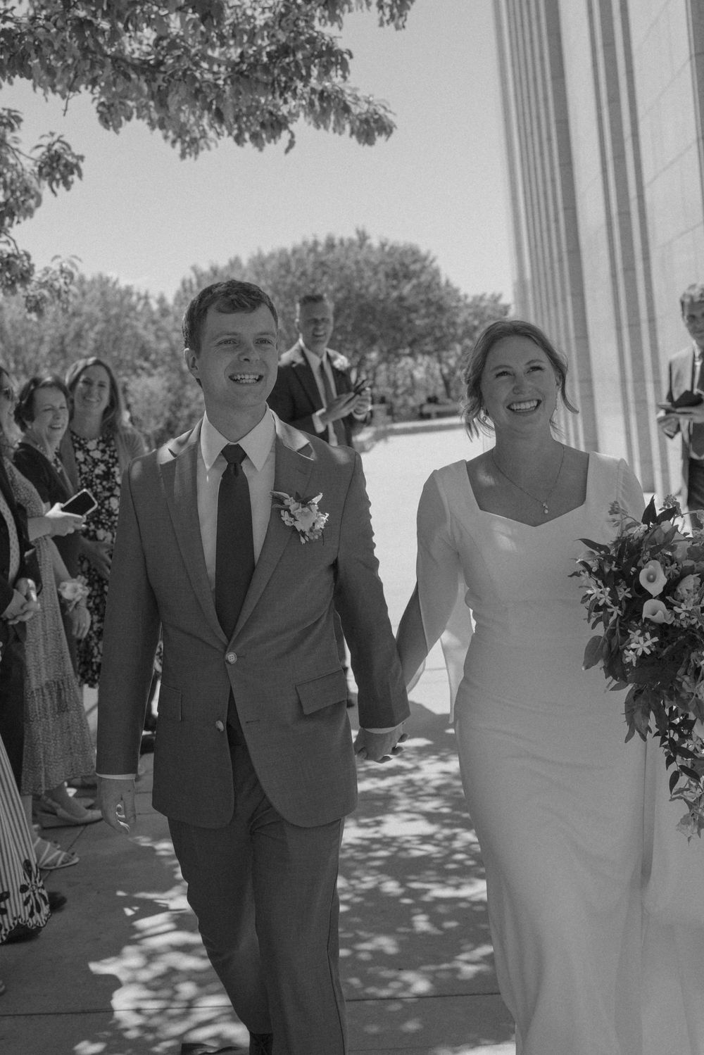Black and white photo of a smiling bride and groom walking down the aisle after their wedding ceremony.