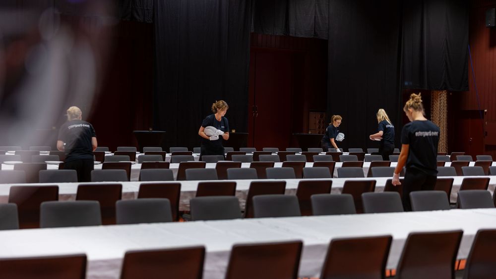 Staff members arranging seats in a large auditorium theater with rows of red chairs during event setup.