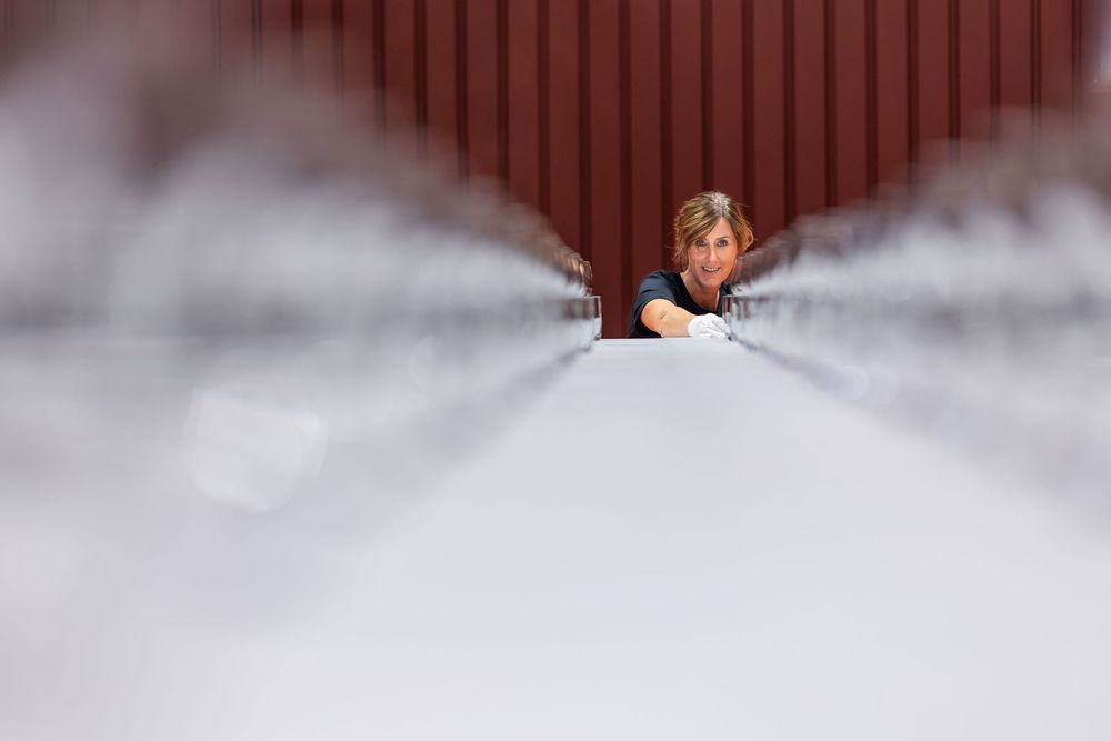 Woman peering over a long white table between red walls in a bright industrial setting.