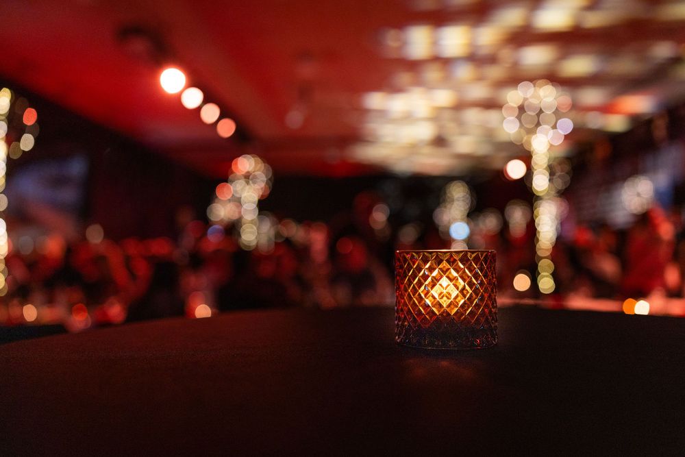 Glowing amber candle holder on dark surface with bokeh lights in background at evening event.
