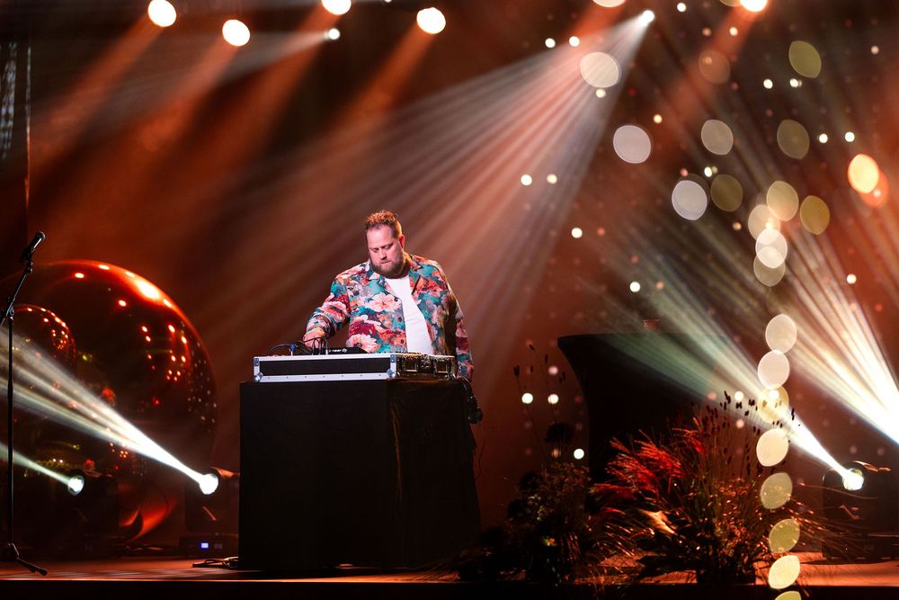 DJ performing on stage under dramatic spotlights and bokeh lighting at a live music event.