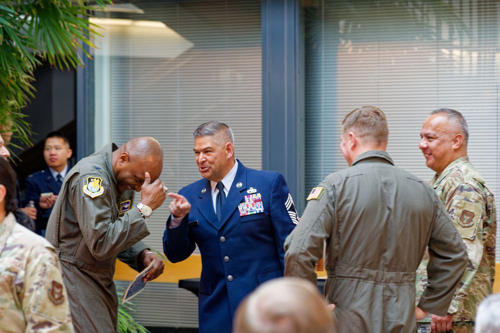 Military officers in dress uniforms and flight suits socialize at an indoor Air Force ceremony.