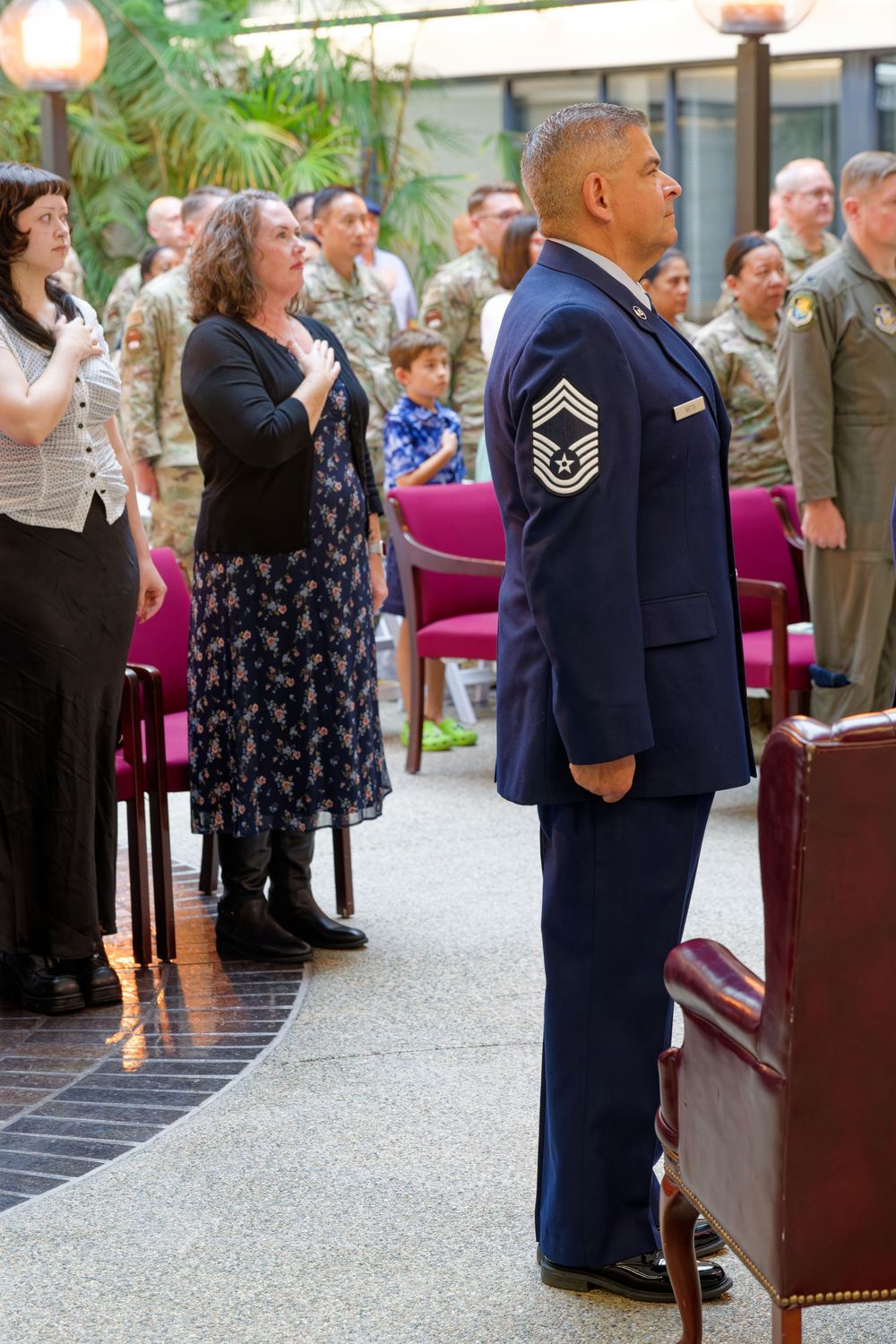 Chief Master Sergeant stands at attention in dress blues during a military ceremony with civilians.