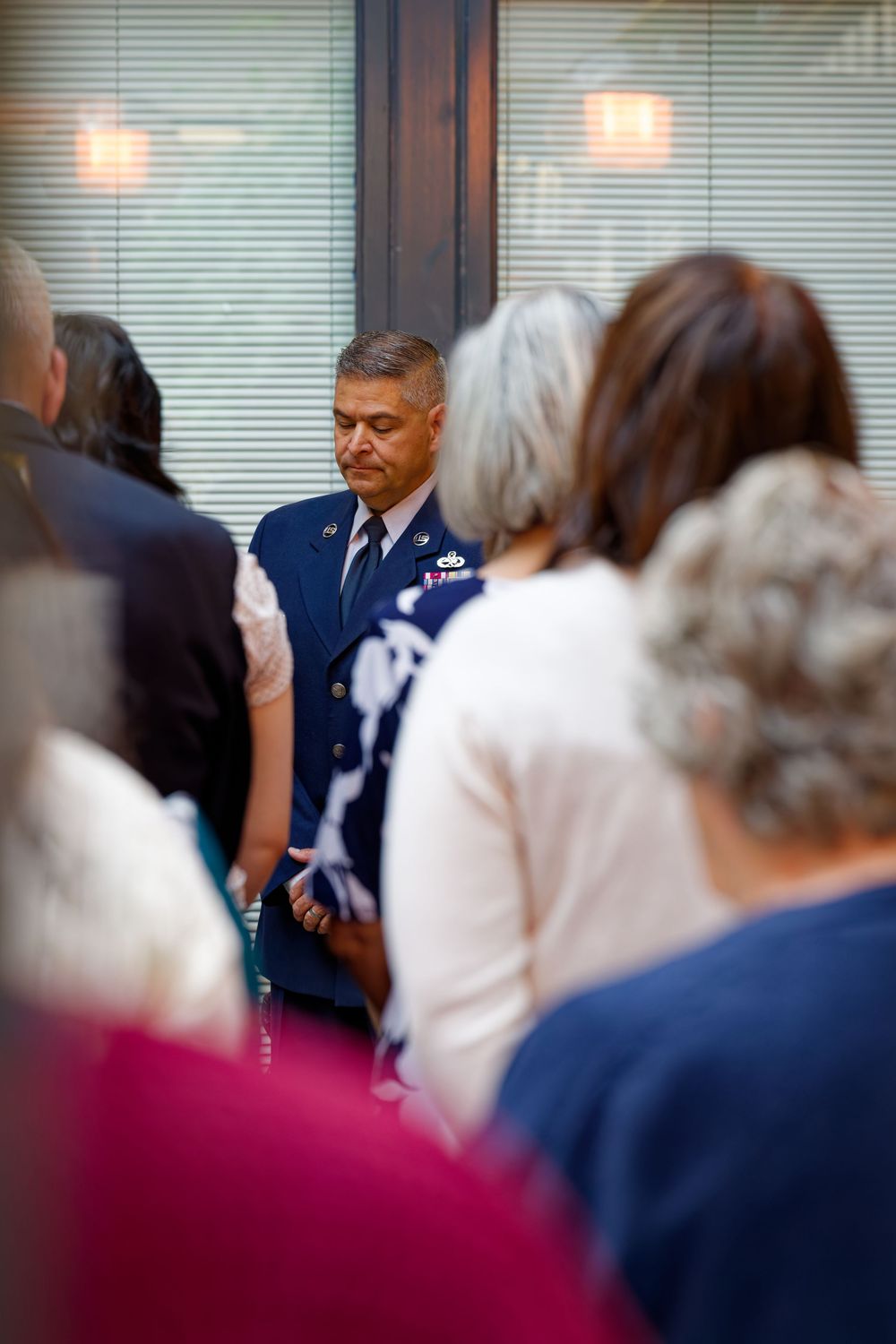 Air Force officer in dress uniform bows head in prayer during a military ceremony.