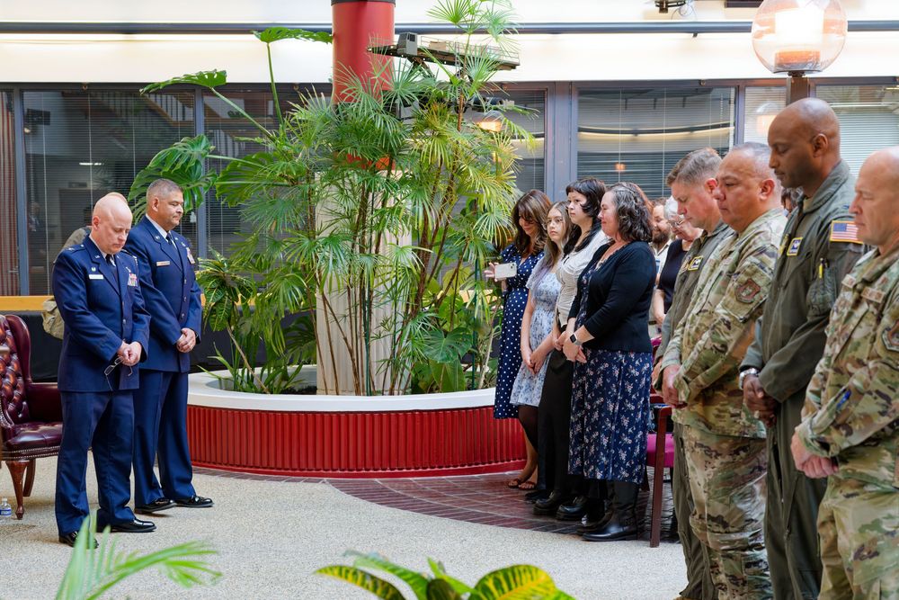 Military personnel and civilians bow heads in prayer during an Air Force ceremony indoors.