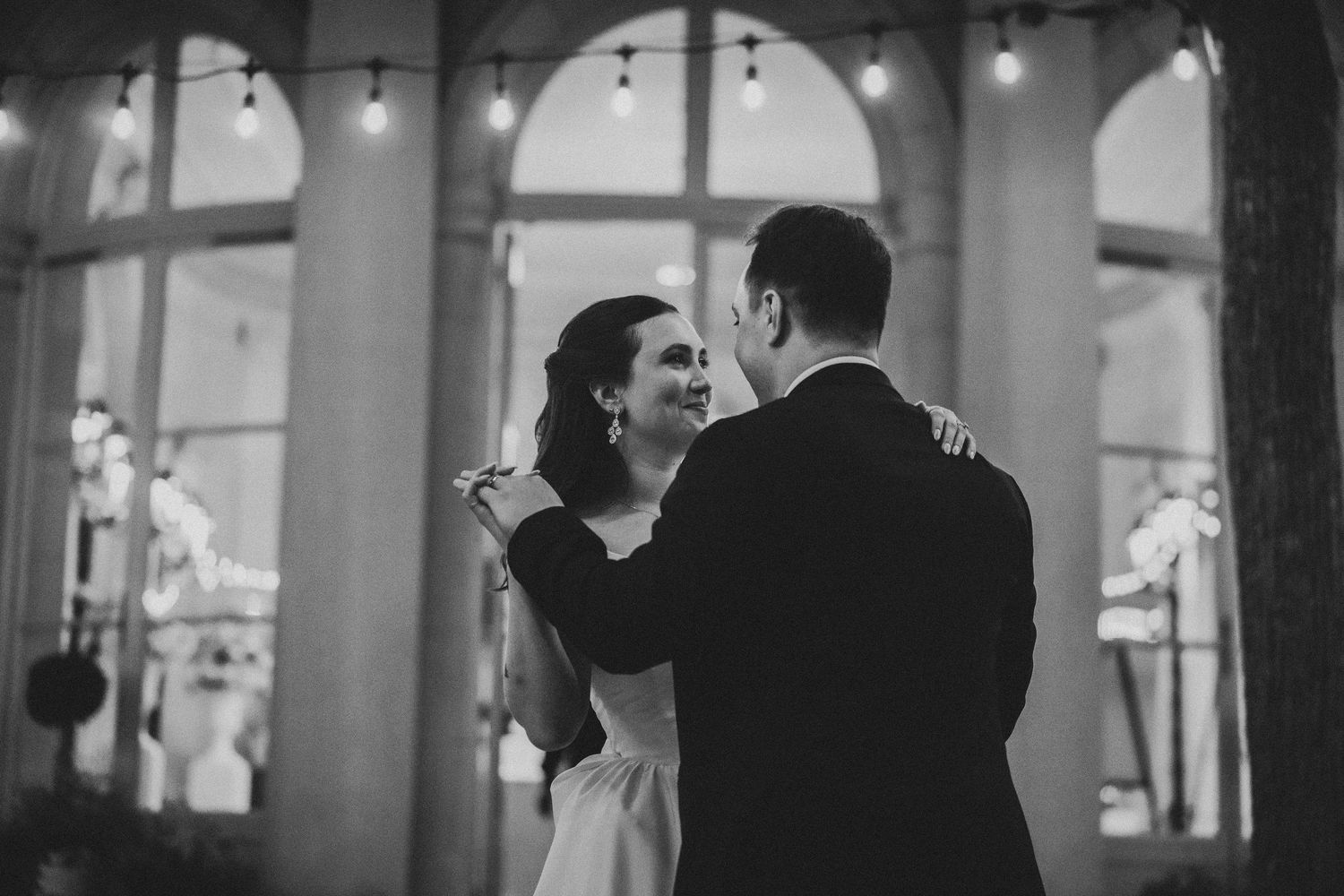 Black and white photo of a bride and groom sharing their first dance at an elegant wedding reception venue.