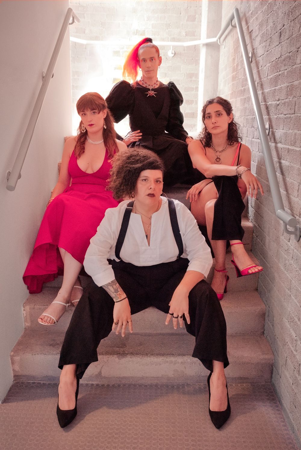 Four stylishly dressed people posing on concrete stairs in a stairwell, wearing formal attire in black, pink, and white.