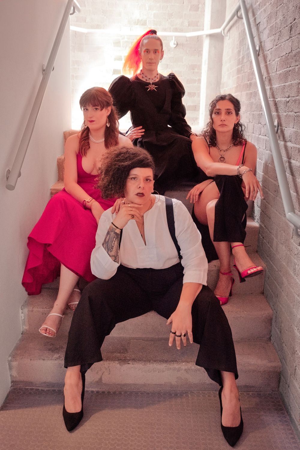 Four stylishly dressed people posing on stairs, wearing elegant outfits in black, white, and pink.