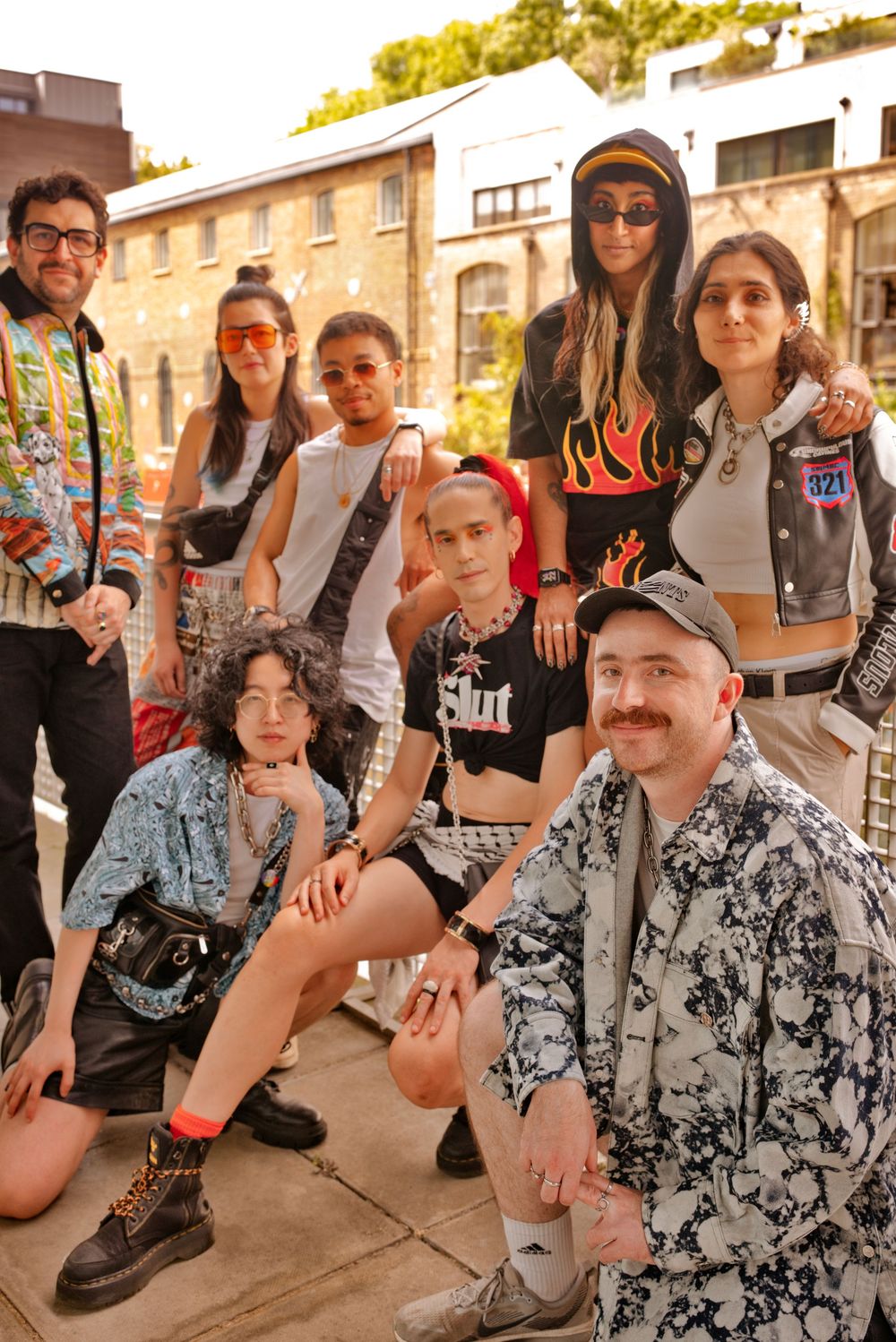 A diverse group of eight stylishly dressed young people posing together outdoors in trendy streetwear fashion.
