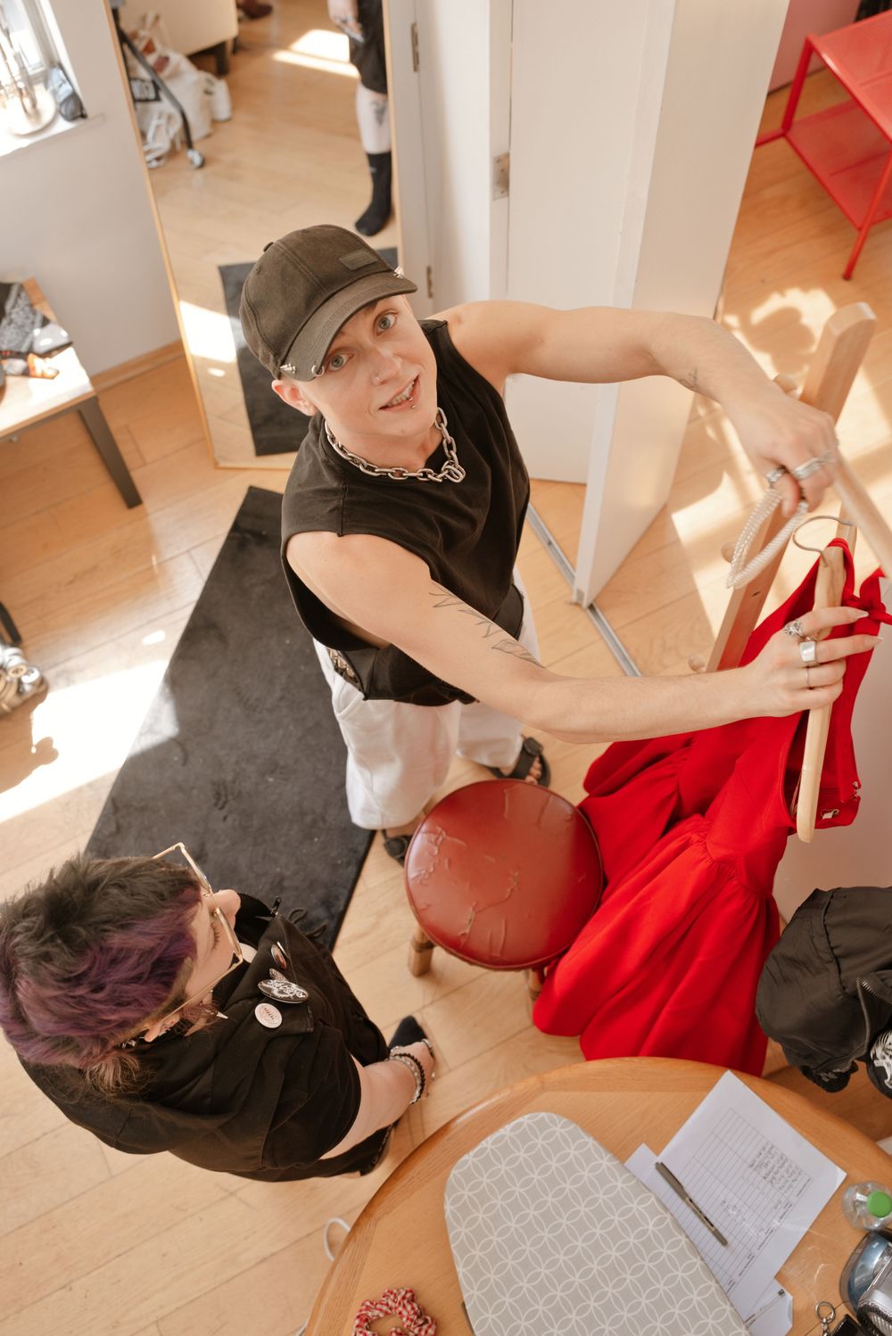 Two people examining a red garment on a rack in a bright boutique store with wooden floors.