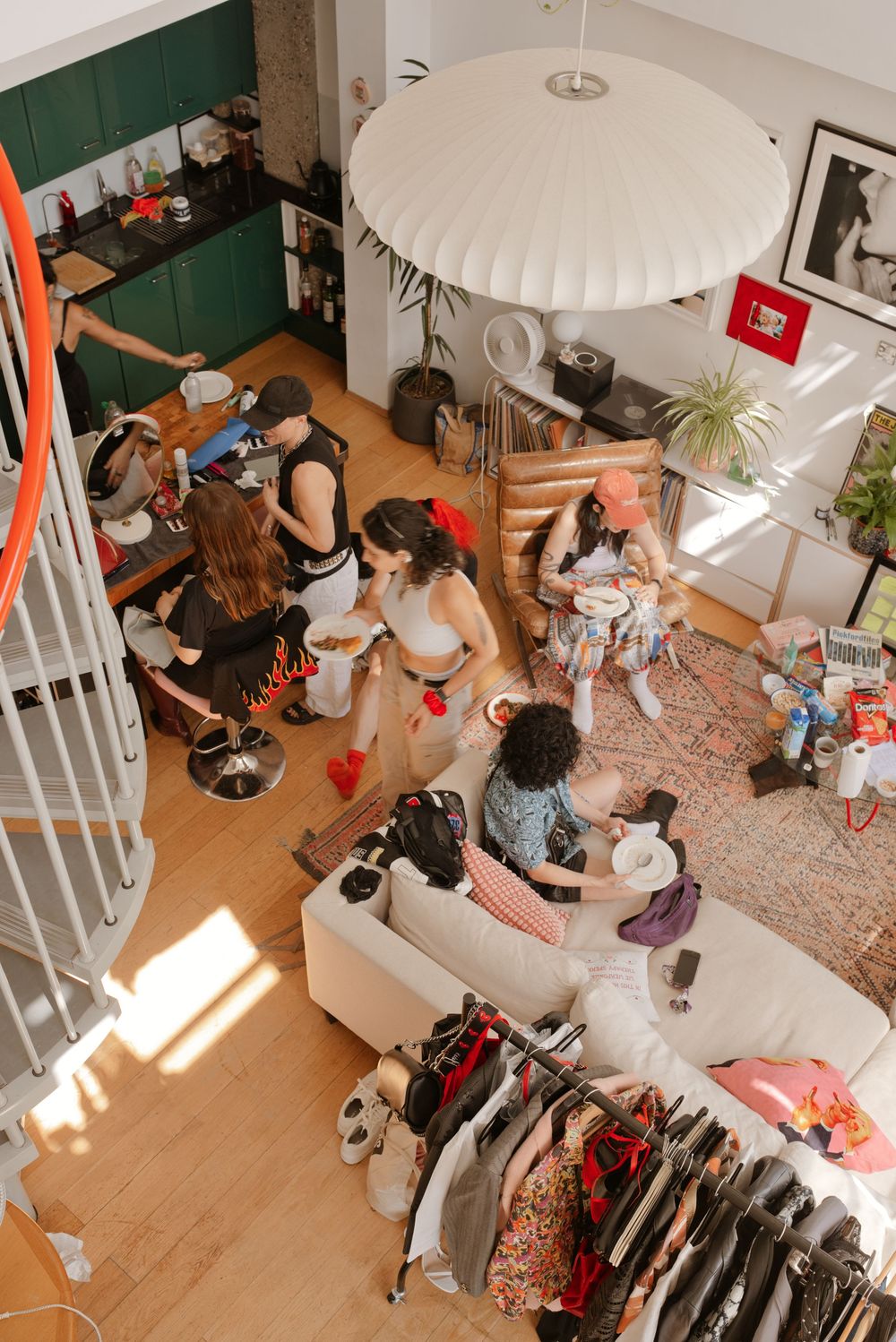 Overhead view of women socializing in a stylish loft apartment with clothing rack, couch, and pendant lamp.